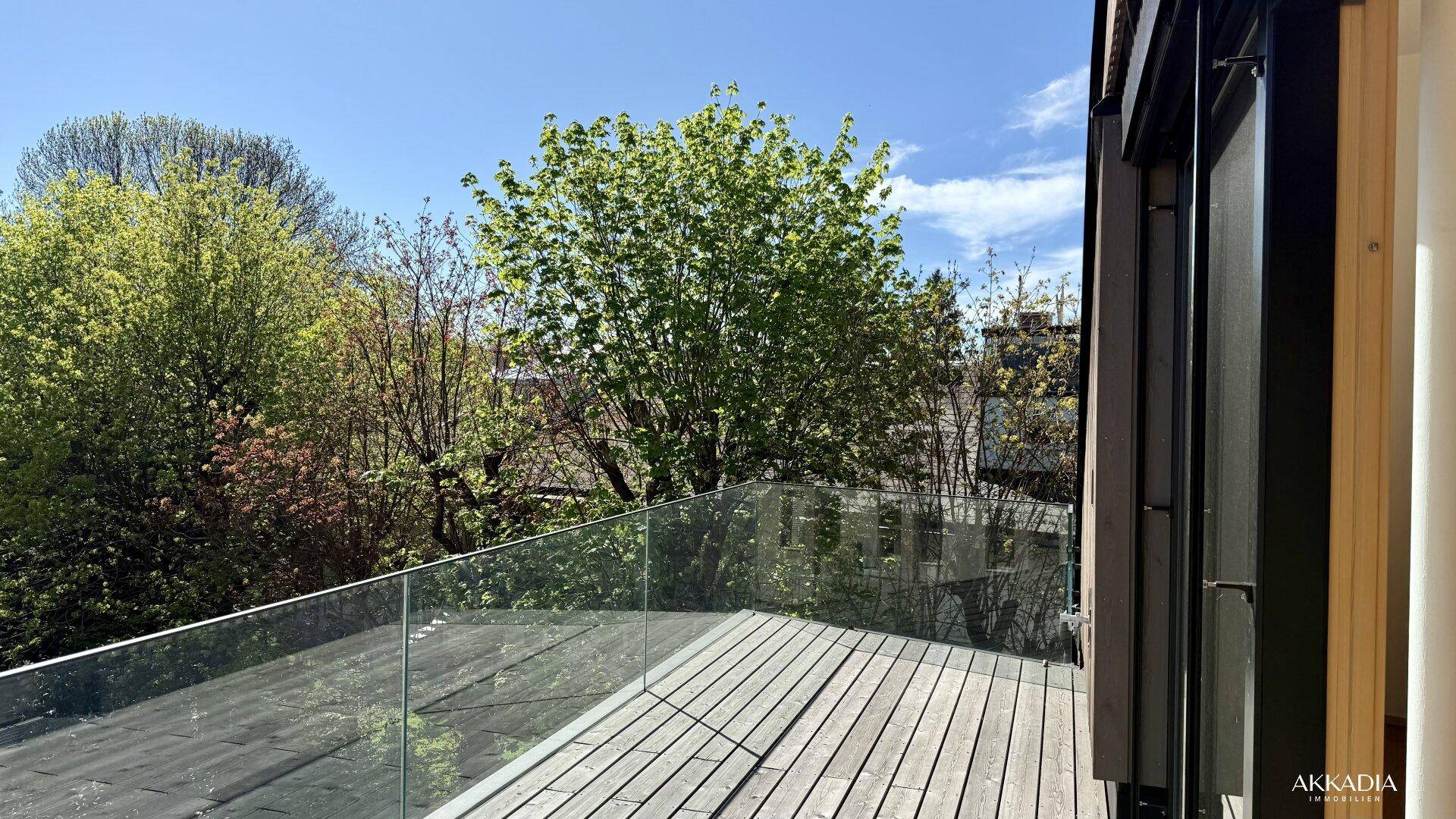 Sonniger Terrassenbereich mit Glasgeländer und üppigem Grünblick.
