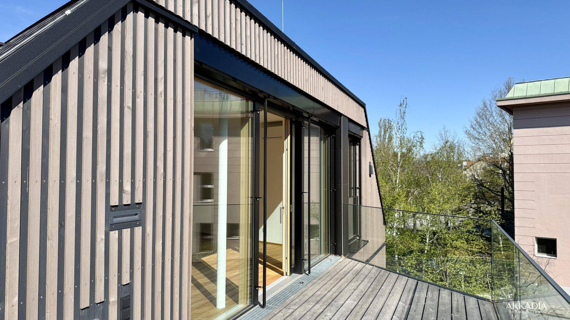 Moderne Holzterrasse mit Glasgeländer und Blick auf die Umgebung.
