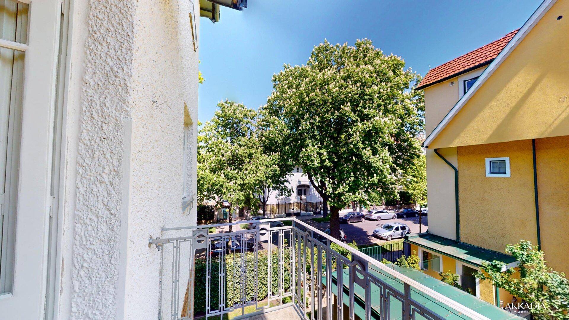 Kleiner Balkon mit Blick auf eine grüne Straße und umliegende Gebäude.