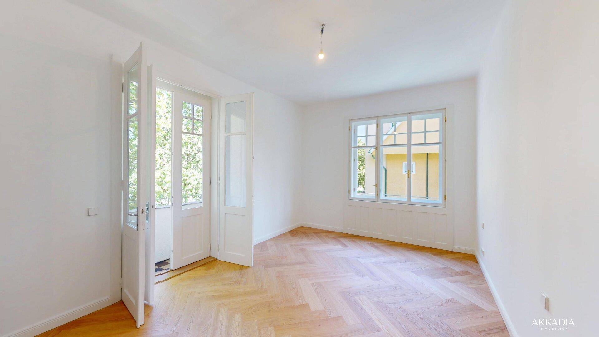 Helles Zimmer mit Fischgrätparkett und Zugang zu einem kleinen Balkon.