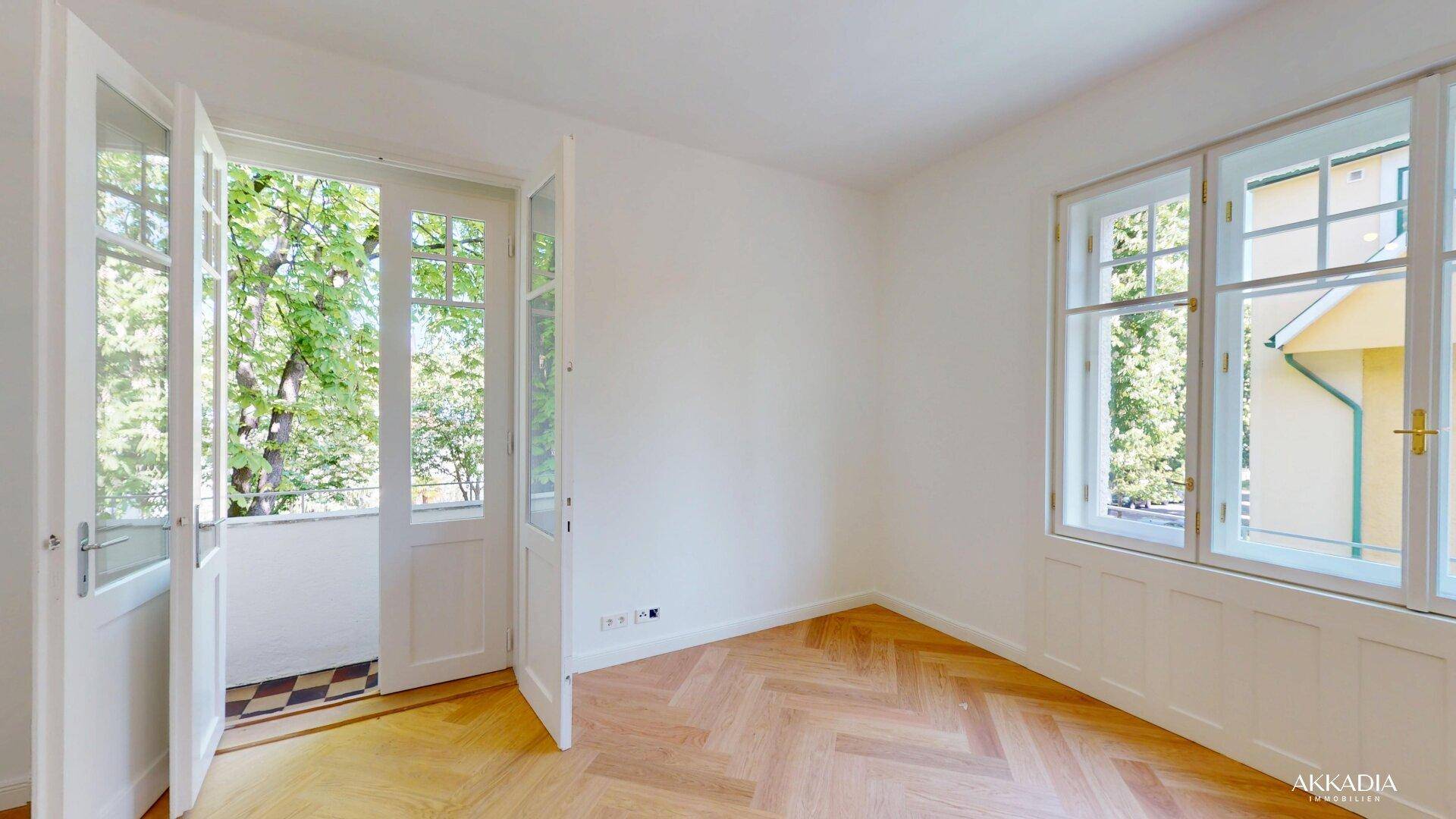 Helles Zimmer mit Fischgrätparkett und Zugang zu einem kleinen Balkon.