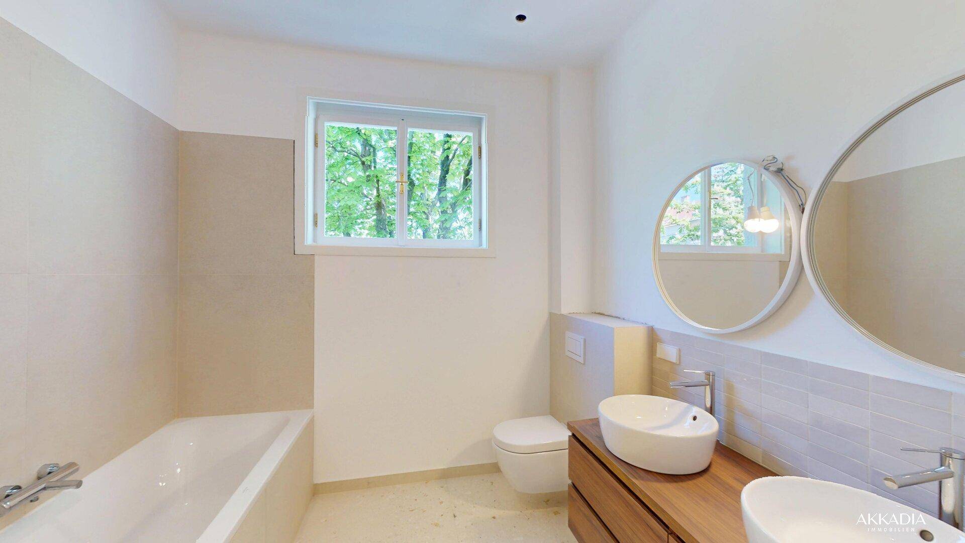 Modernes Badezimmer mit Doppelwaschbecken, Badewanne und Fenster mit Blick ins Grüne.