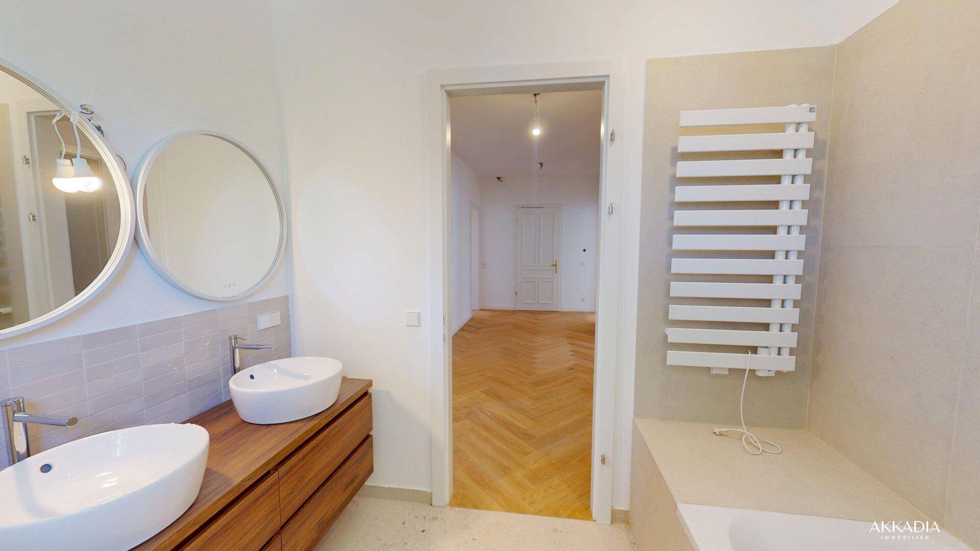 Modernes Badezimmer mit Doppelwaschbecken, beheiztem Handtuchhalter und Zugang zum Flur.