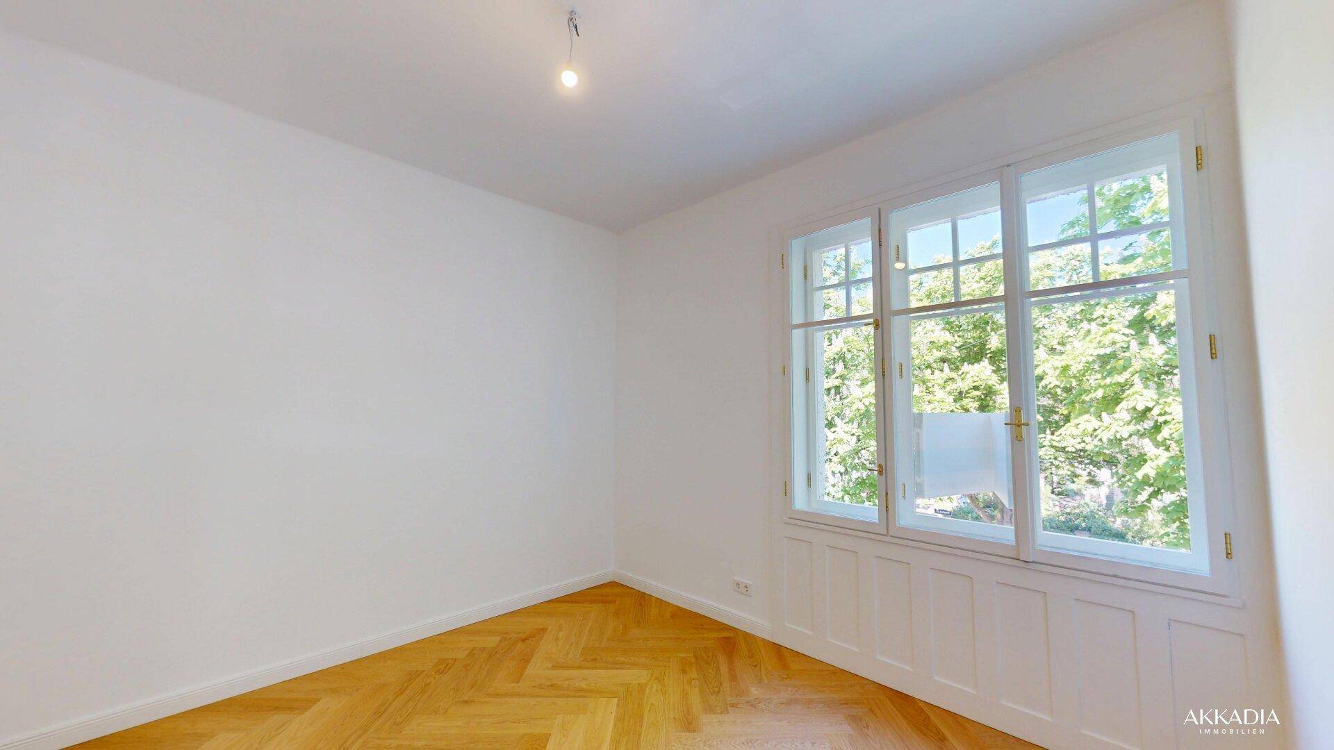 Helles Zimmer mit Fischgrätparkett und großen Fenstern mit Blick ins Grüne.
