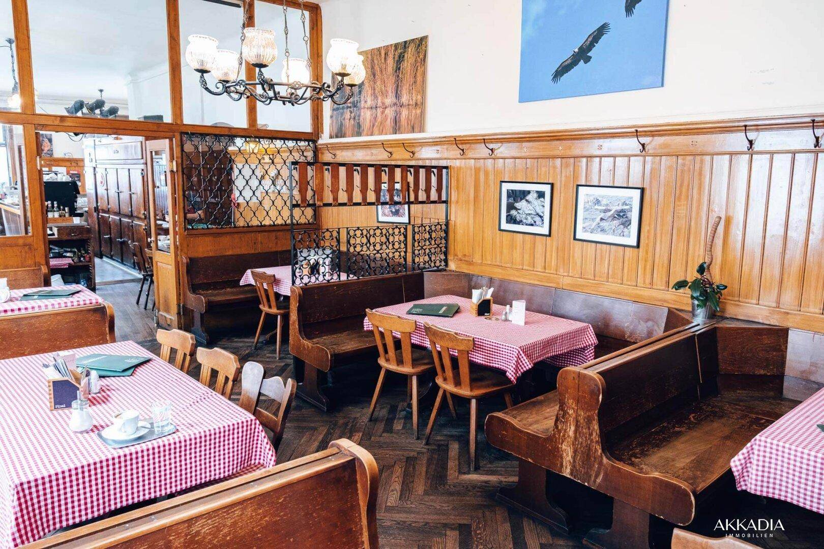 Ein traditioneller Gastraum mit Holztäfelung, Bänken und Tischen mit rot-weiß karierten Decken.