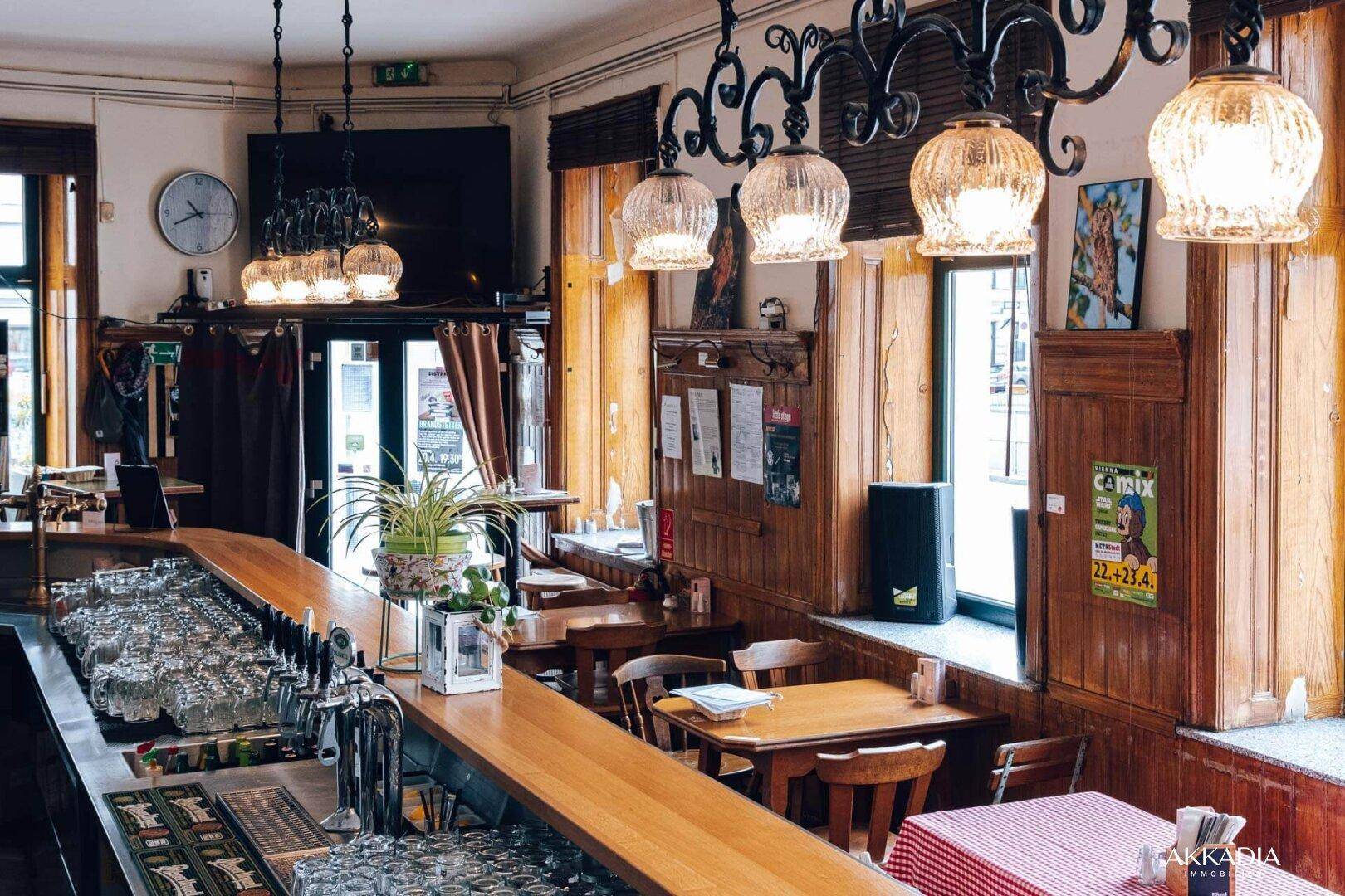 Eine gut beleuchtete Bar mit Holztresen, vielen Gläsern und traditionellen Hängelampen.