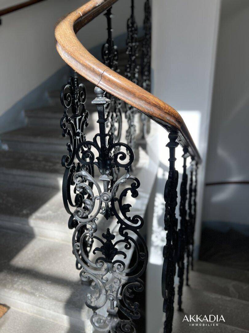 Detailaufnahme eines kunstvoll geschmiedeten Treppengeländers mit Holzhandlauf in einem Altbau.