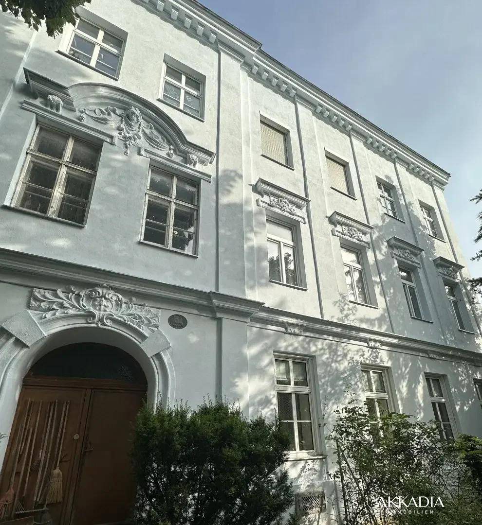 Ehrwürdige Altbaufassade mit dekorativen Stuckelementen und klassischen Fenstern unter blauem Himmel.