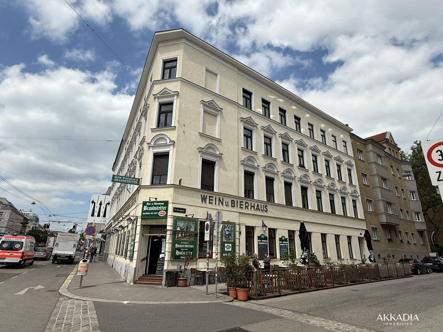 Ein großes Eckgebäude mit einem Wein- und Bierhaus im Erdgeschoss, an einer städtischen Kreuzung.