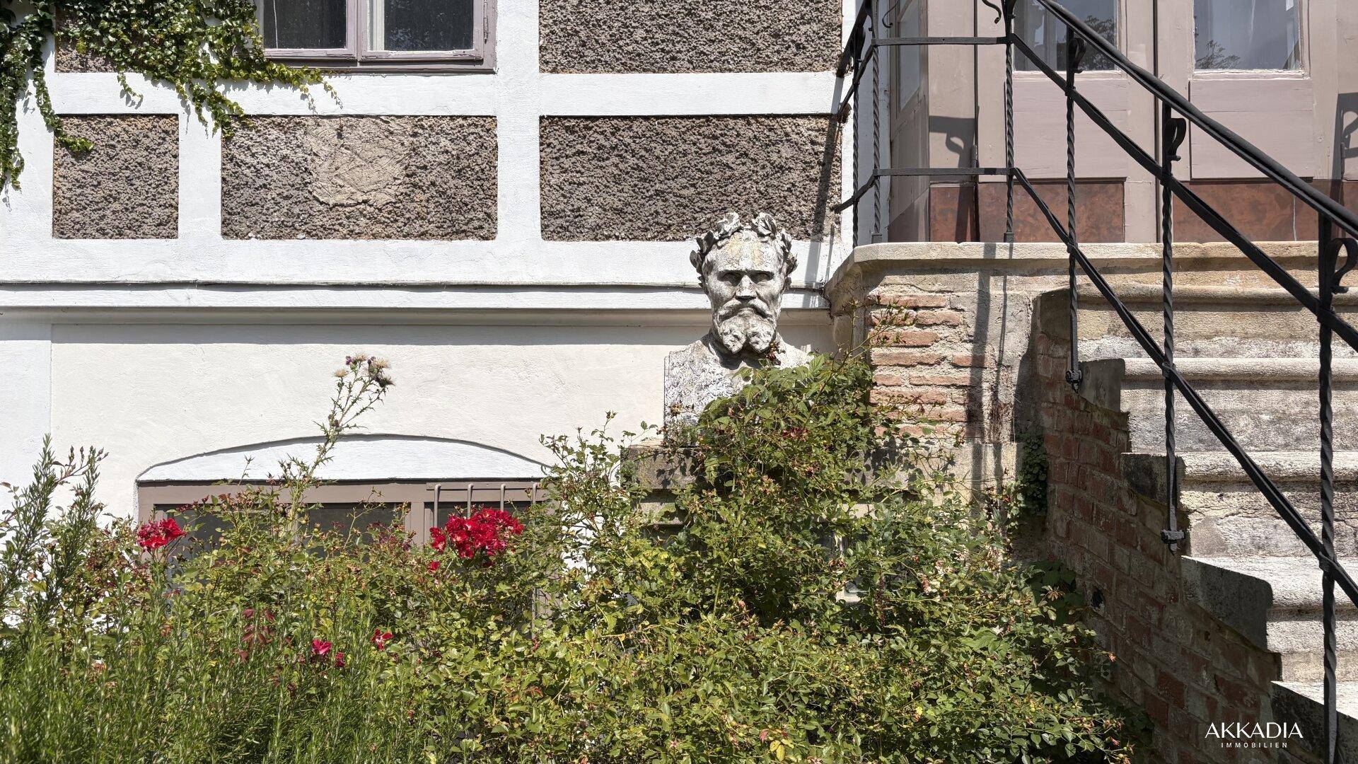 Detailansicht einer historischen Büste im Gartenbereich vor der Fassade des Gebäudes.