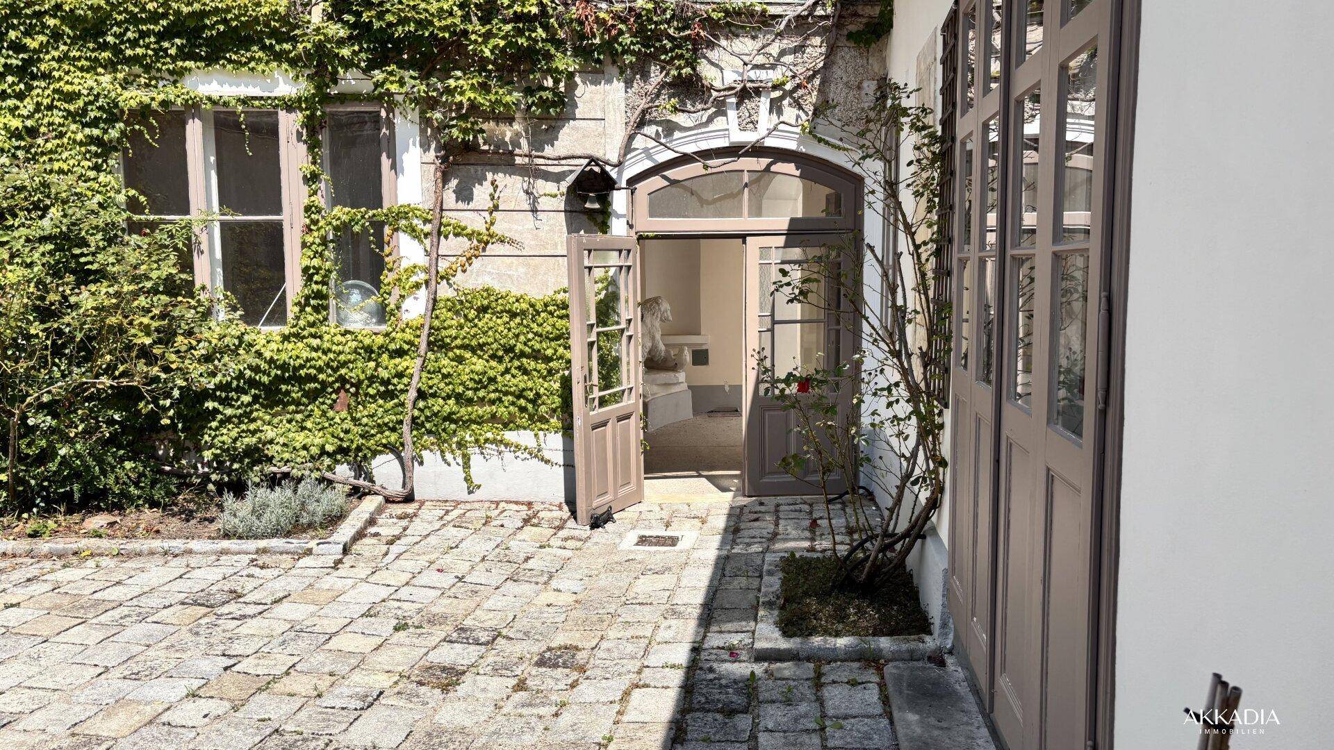Gepflasterter Innenhof mit offenstehender Tür, die den Blick in den Innenbereich freigibt.