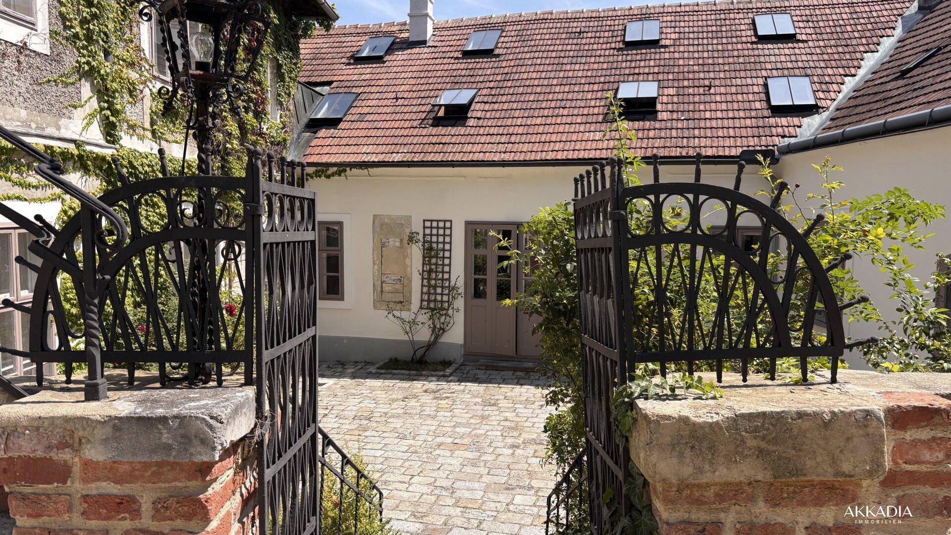 Blick durch ein schmiedeeisernes Tor auf den gepflasterten Innenhof und die historischen Gebäude.
