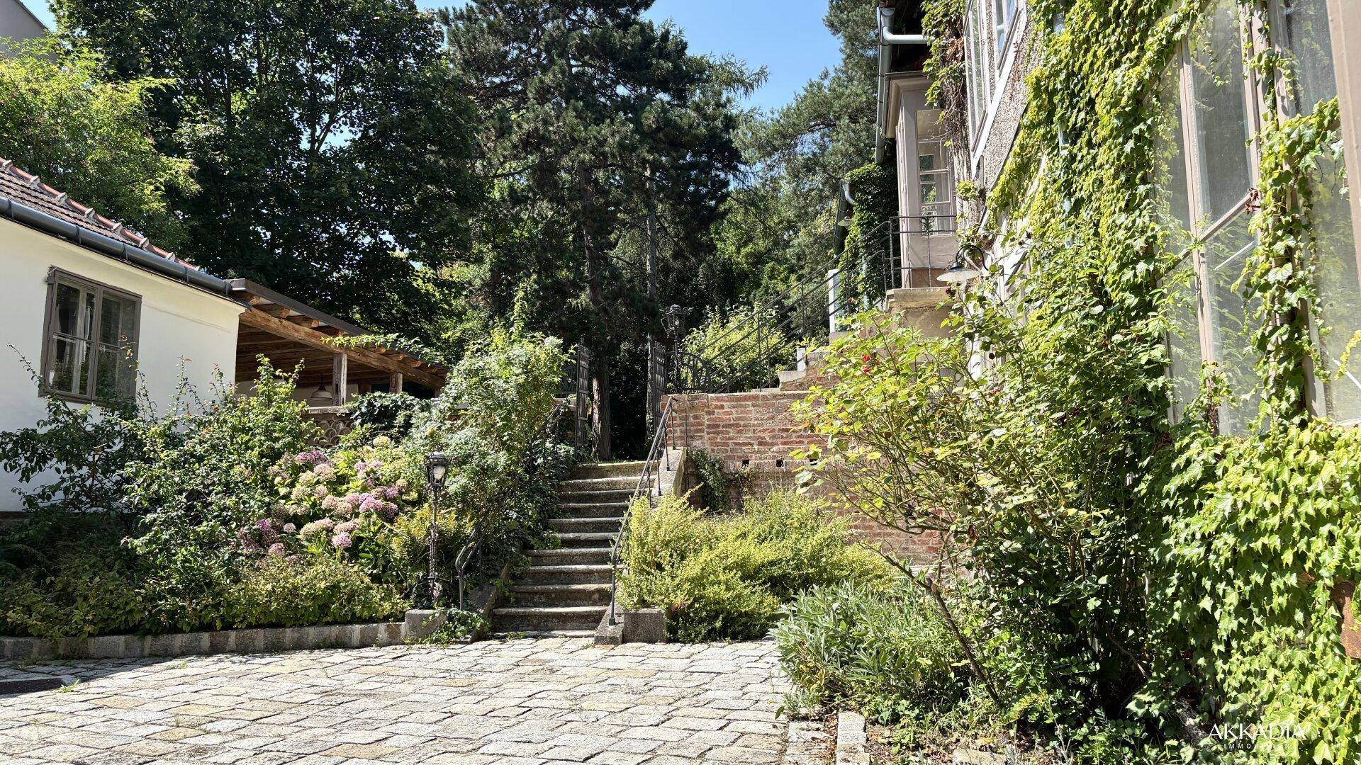 Gepflasterter Innenhof mit Steintreppe, die zu einem höher gelegenen Gartenbereich führt.