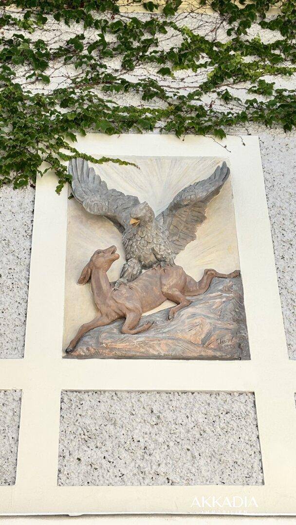 Detailansicht eines Wandgemäldes mit einem Adler und einem Hirsch, umgeben von Efeu.