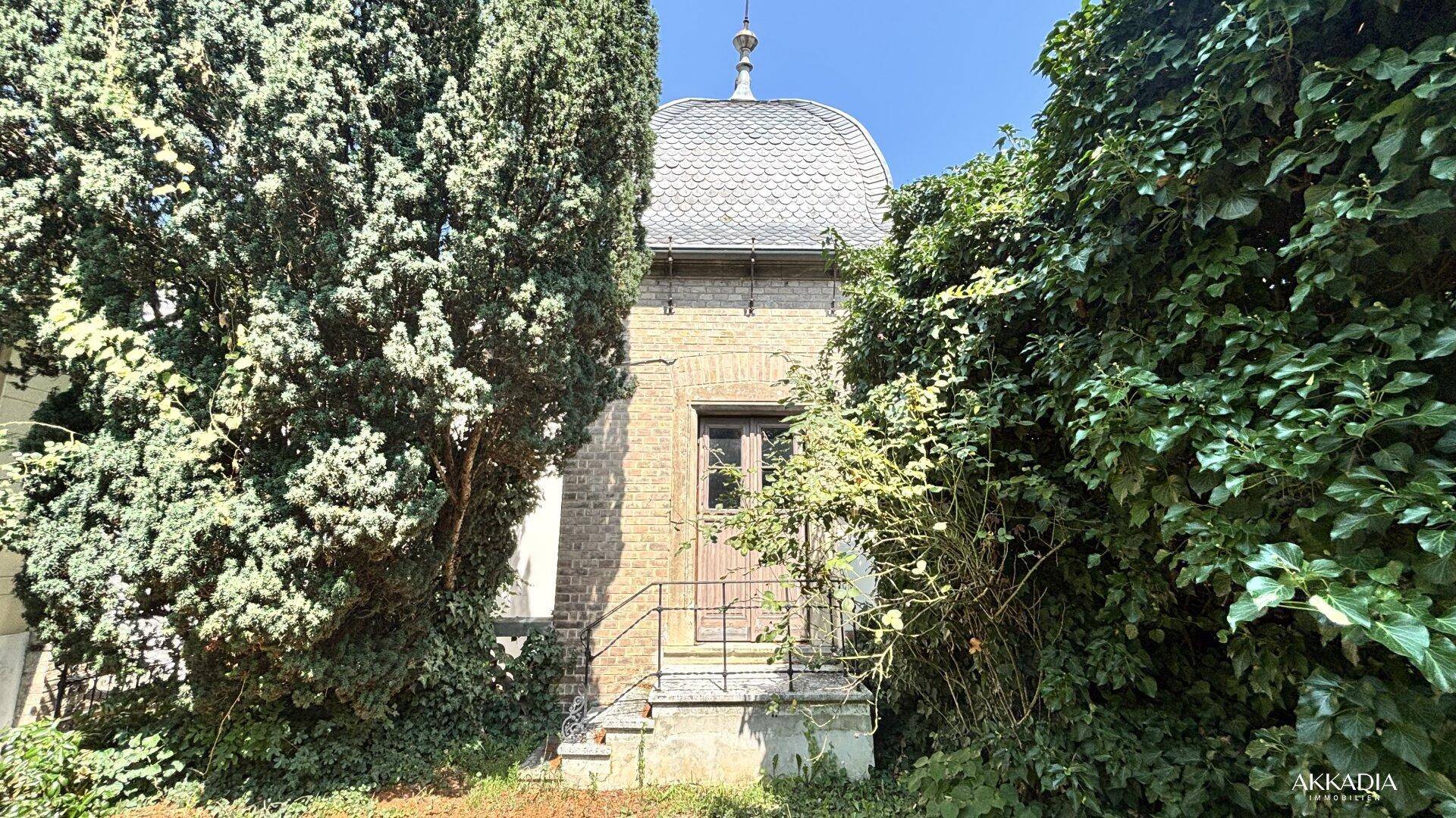 Kleines, charmantes Gebäude mit Kuppeldach, umgeben von dichtem Grün im Garten.