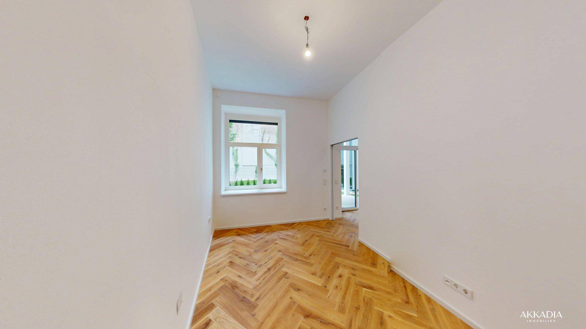 Helles Zimmer mit Fischgrätparkett und einem Fenster, das viel Tageslicht hereinlässt.