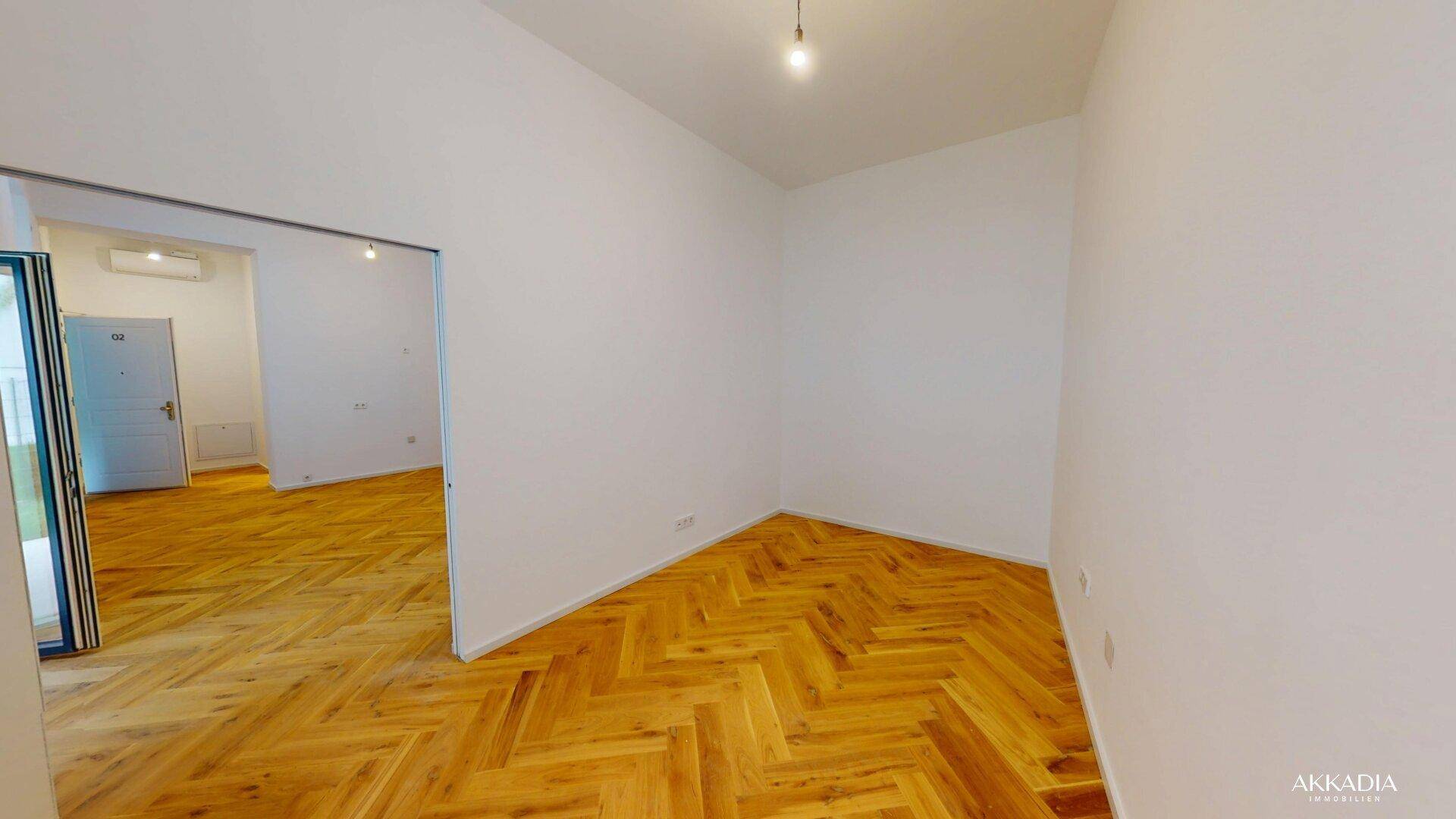 Geräumiges Zimmer mit elegantem Fischgrätparkett und offenem Übergang zu weiteren Räumen.