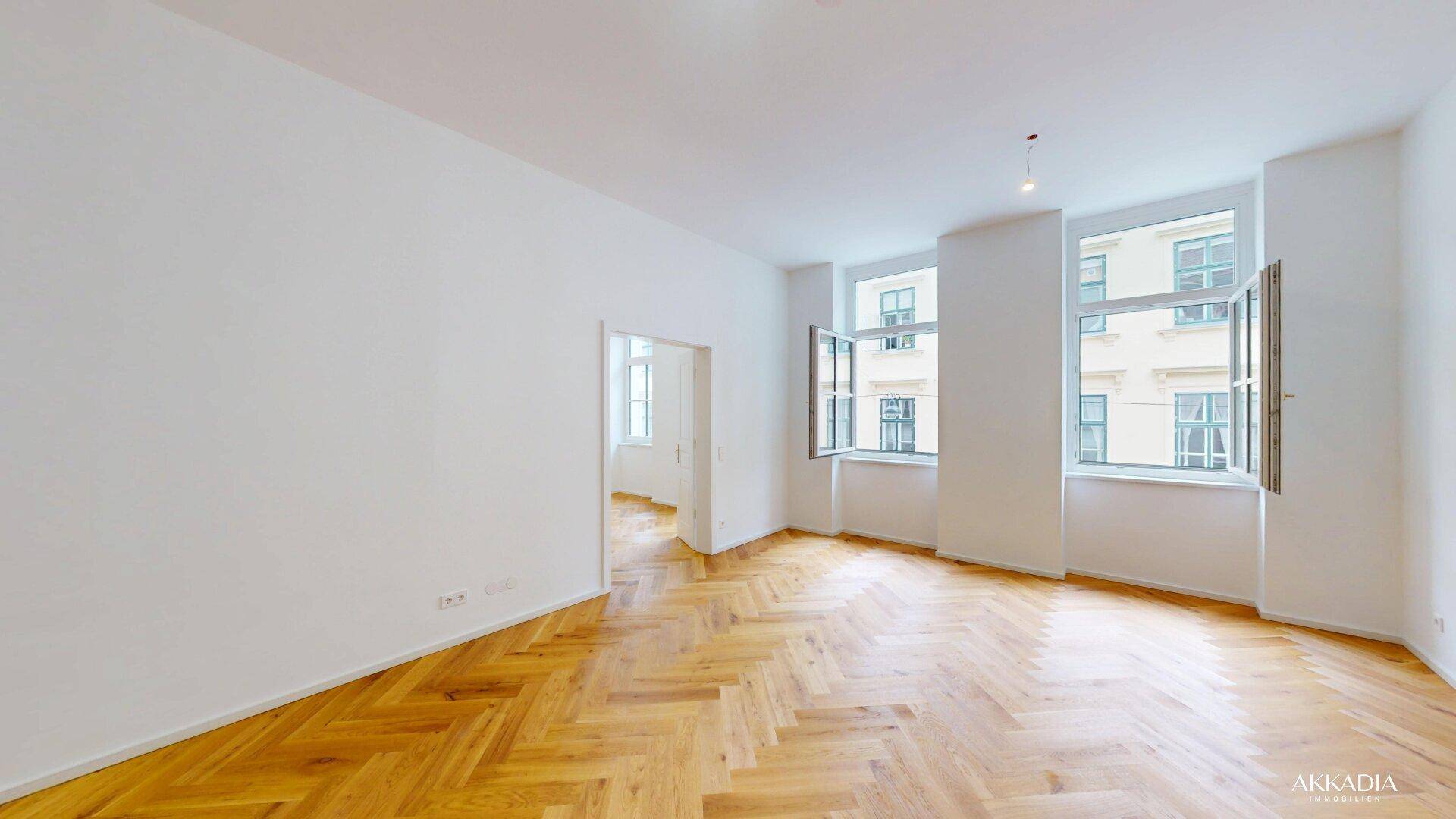 Heller Wohnraum mit mehreren Fenstern und elegantem Fischgrätparkett, ideal für natürliches Licht.