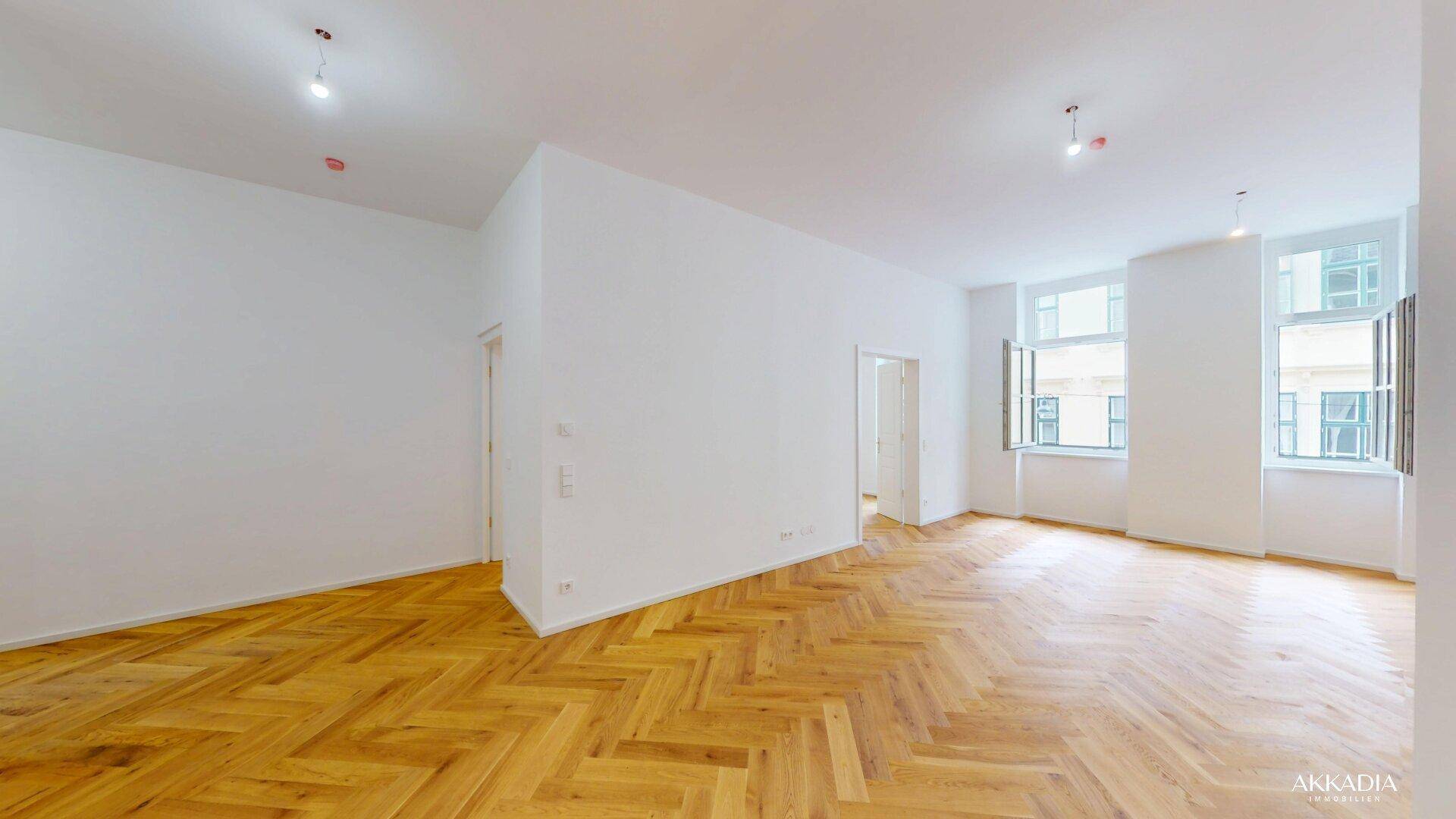 Weitläufiger Raum mit klassischem Fischgrätparkett und hohen Decken, bereit für neue Bewohner.