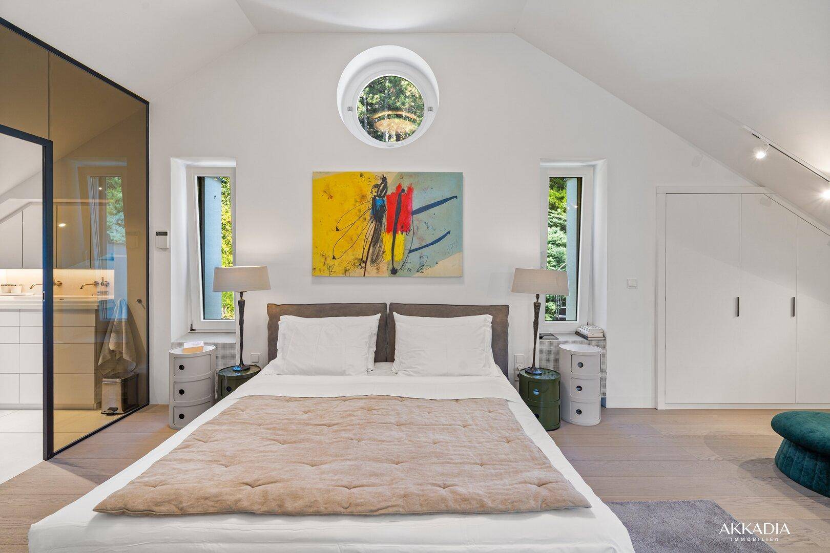 Helles Schlafzimmer im Dachgeschoss mit runden und hohen Fenstern sowie moderner Kunst.