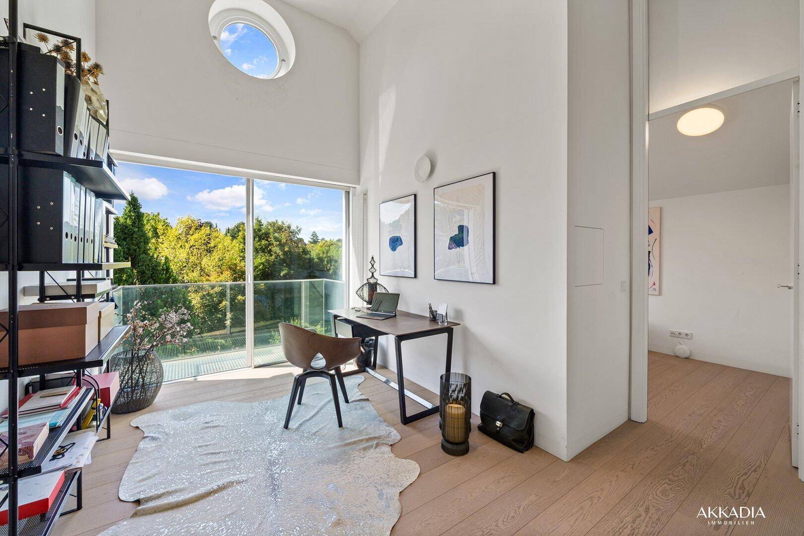 Helles Arbeitszimmer mit großen Fenstern, die Zugang zu einem Balkon und Blick ins Grüne bieten.