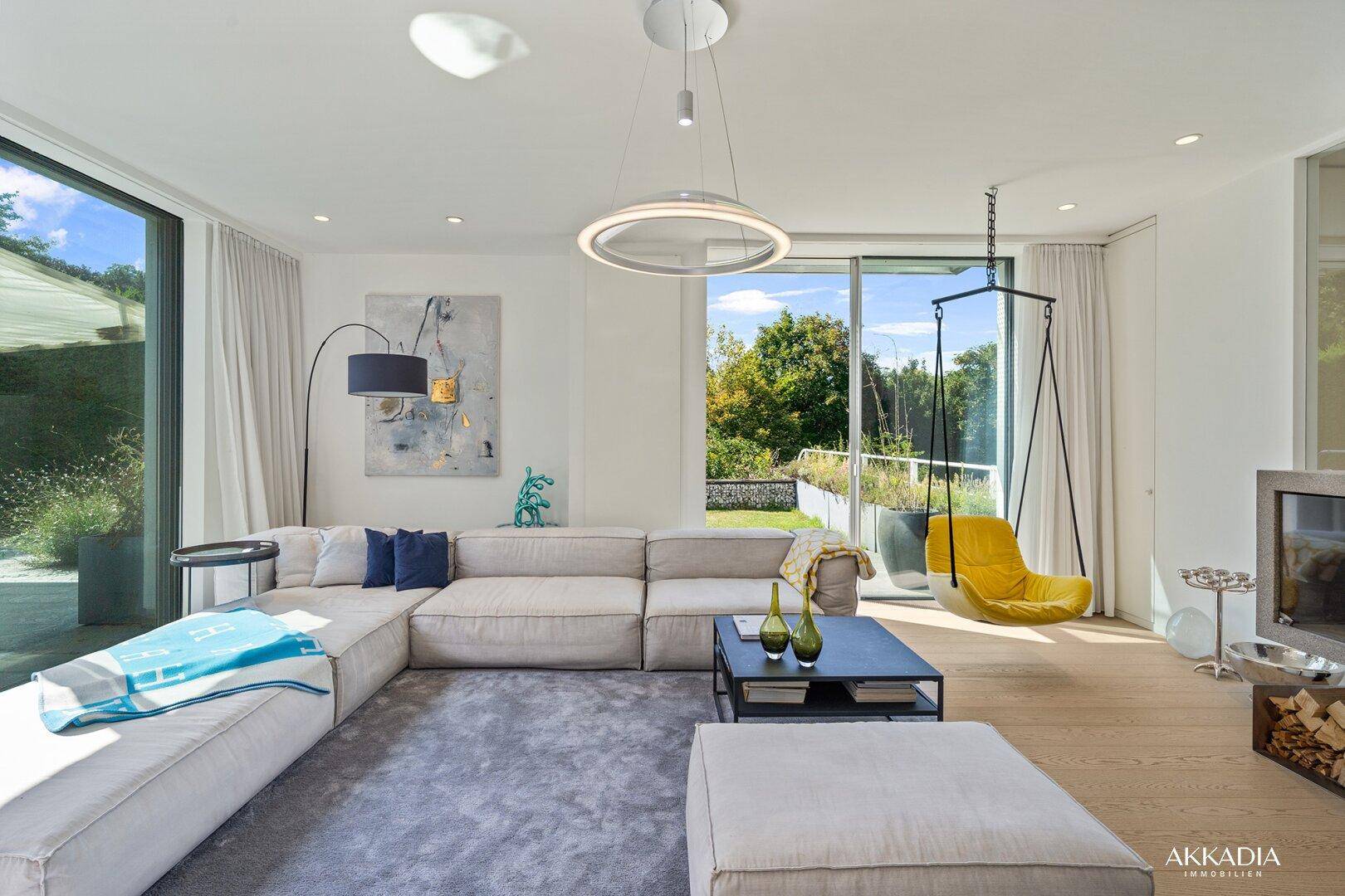 Helles Wohnzimmer mit großem Sofa, Holzboden und weitem Blick in den grünen Garten.