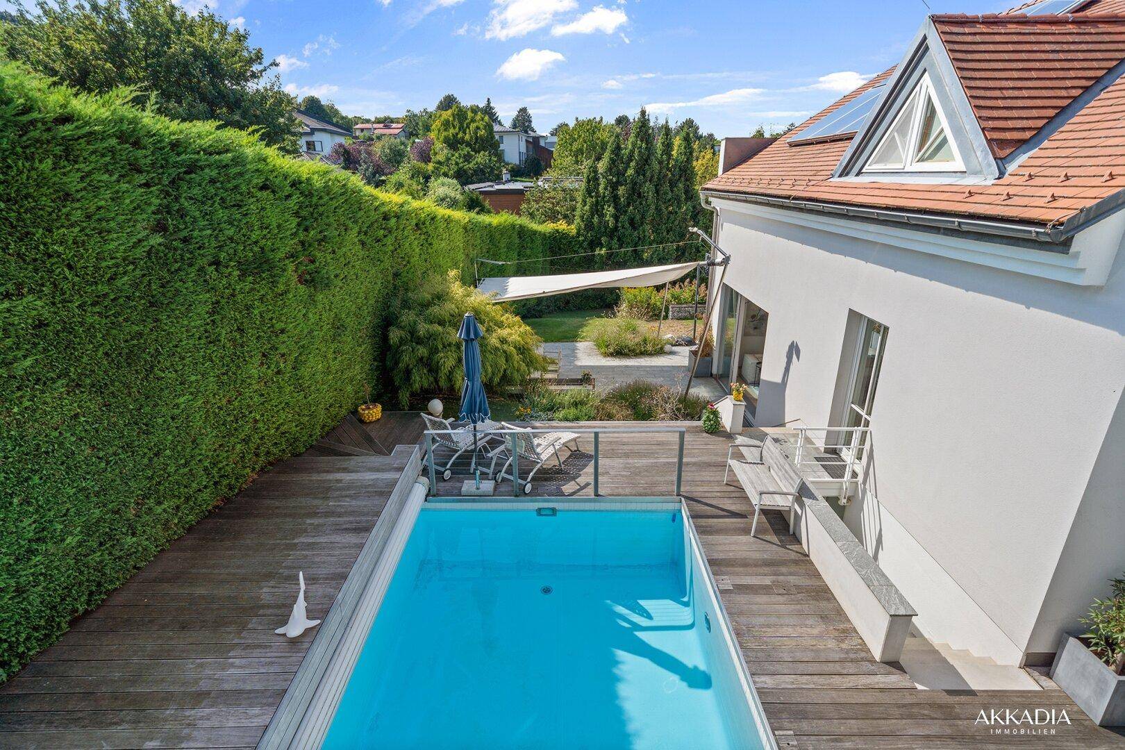 Außenbereich mit Pool, Holzdeck und gepflegter Hecke, umgeben von viel Grün.