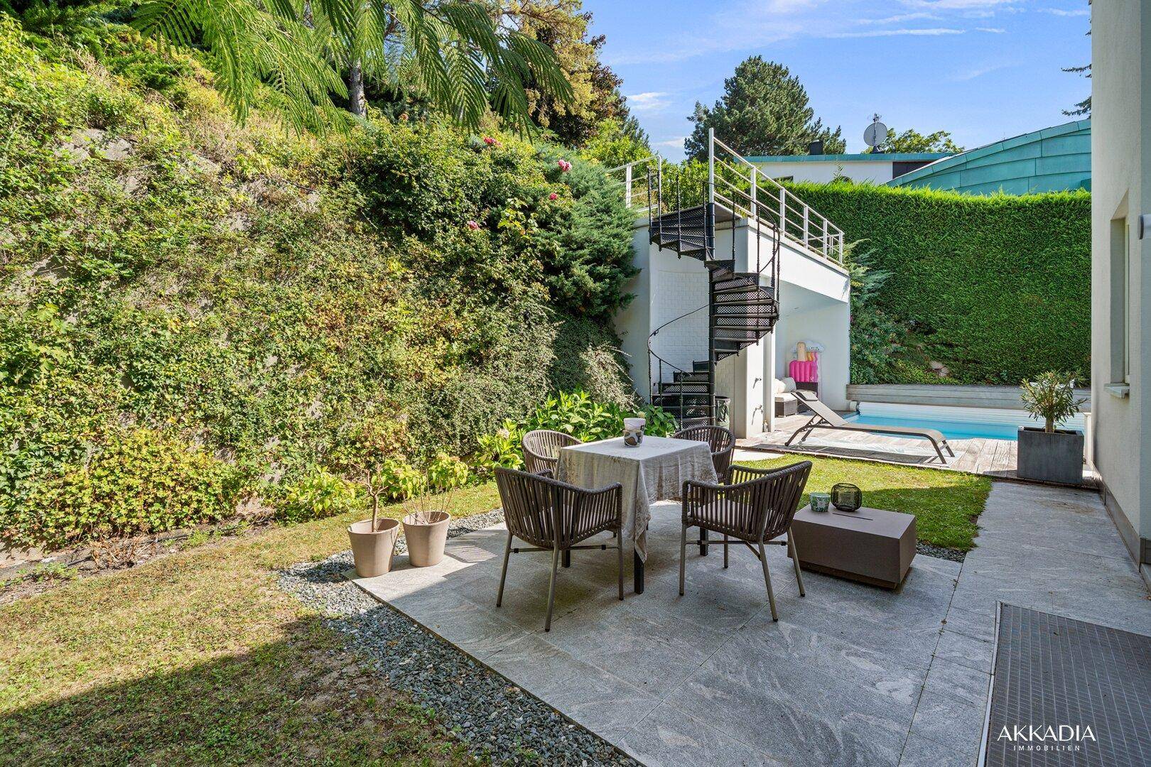Gepflegter Garten mit Sitzbereich, Rasenfläche und Wendeltreppe zu einer oberen Ebene.