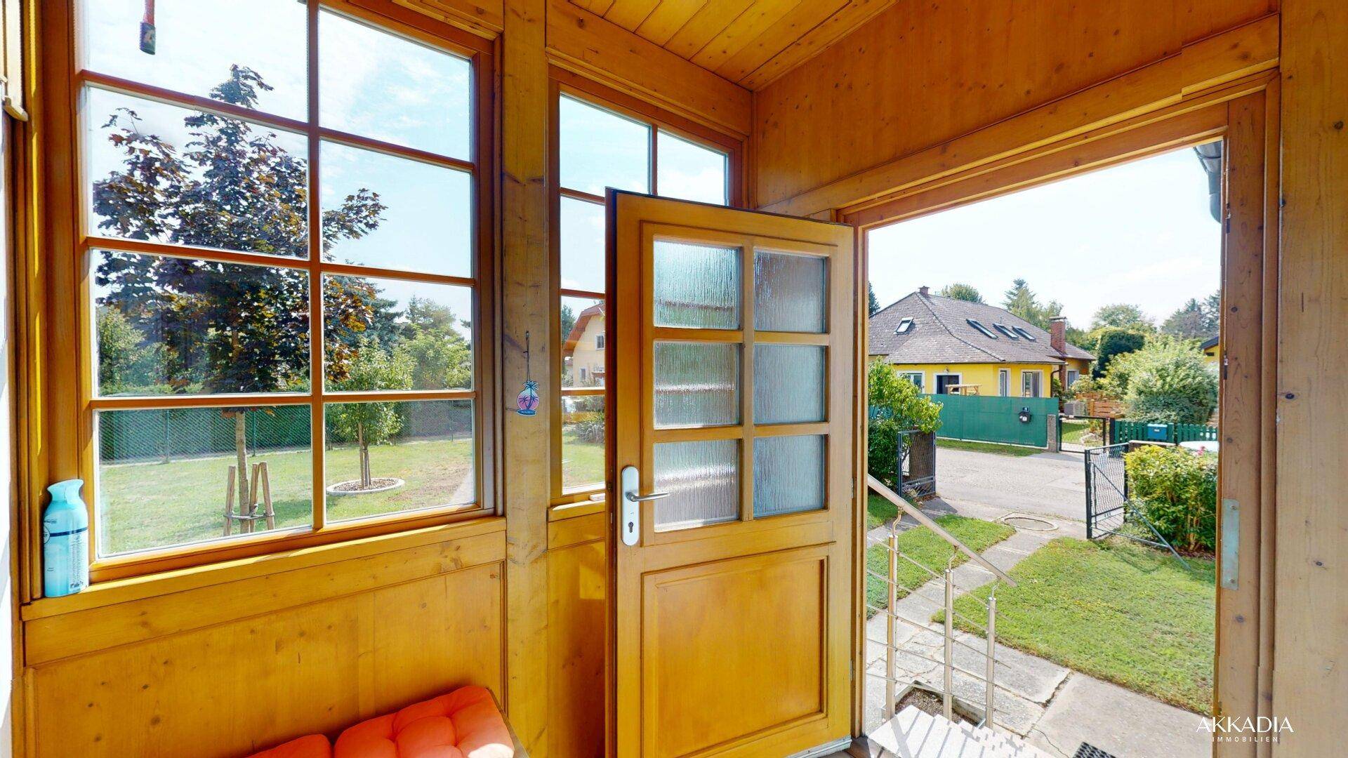 Eingangsbereich mit Holzvertäfelung, großen Fenstern und Blick auf den Vorgarten und die Straße.