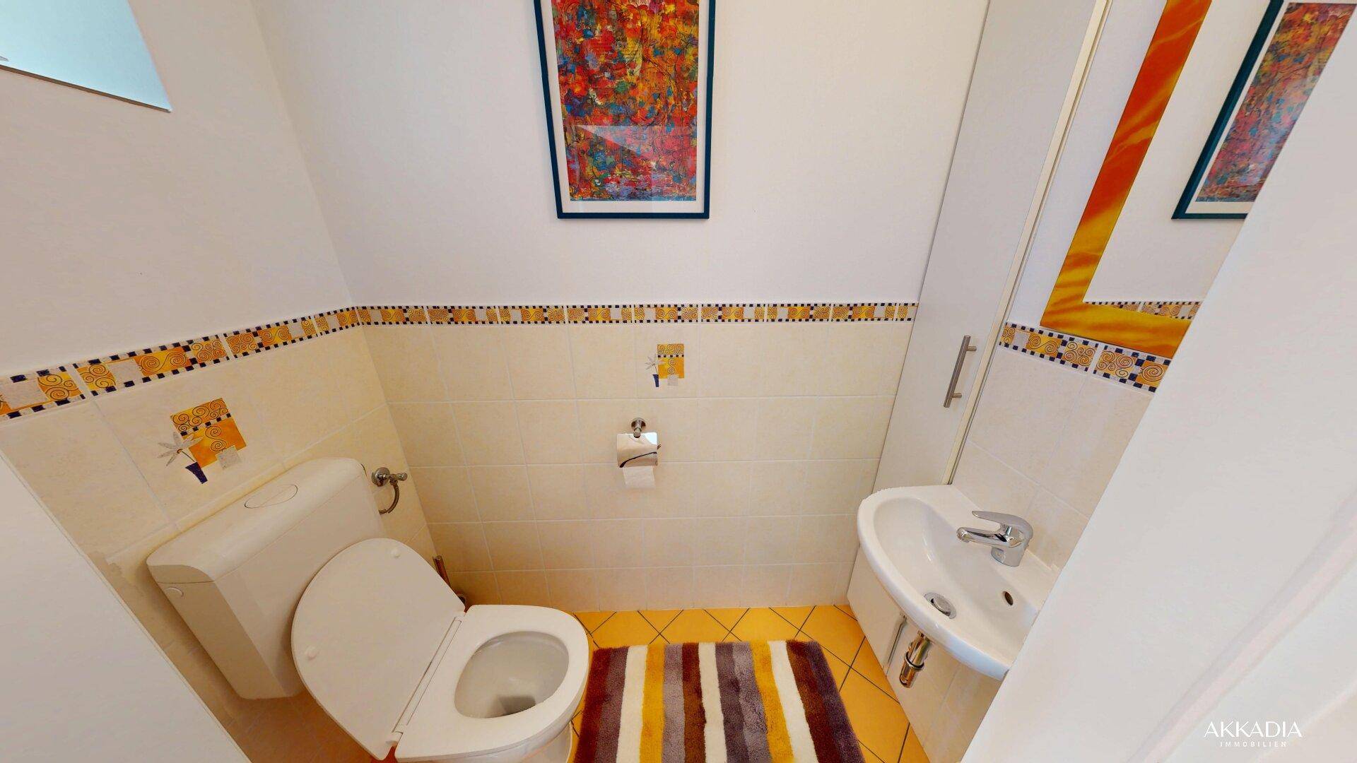 Kleines Gäste-WC mit WC, Waschbecken und farbigen Fliesenakzenten.