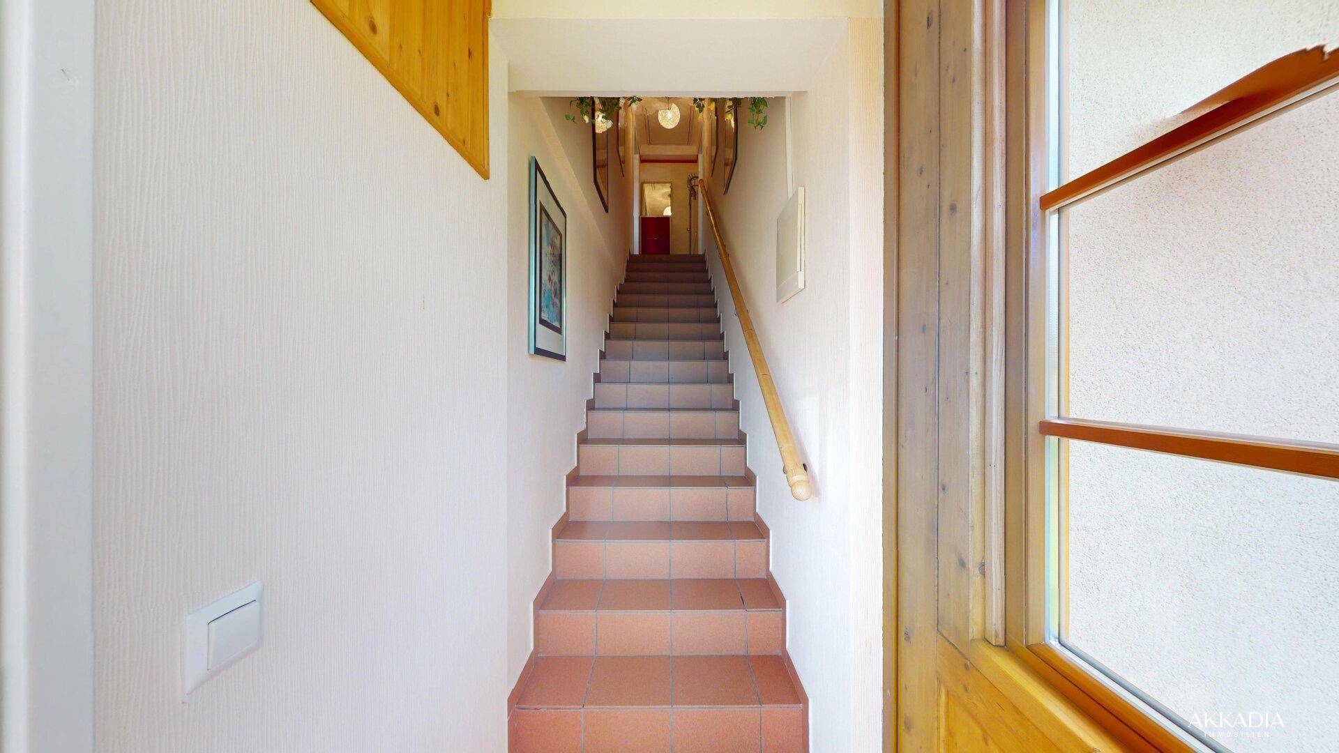 Treppenhaus mit Holzgeländer und Terrakotta-Fliesen, führt in die obere Etage.