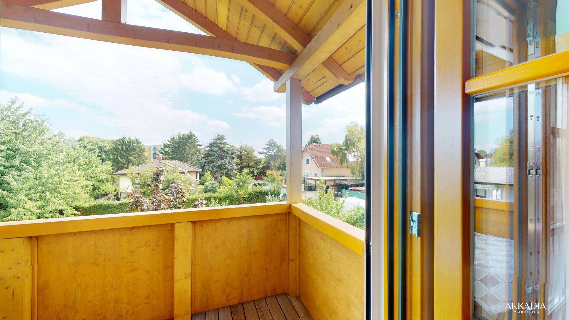 Sonniger Holzbalkon mit Blick auf den grünen Garten und die umliegende Wohngegend, ideal zum Entspannen.