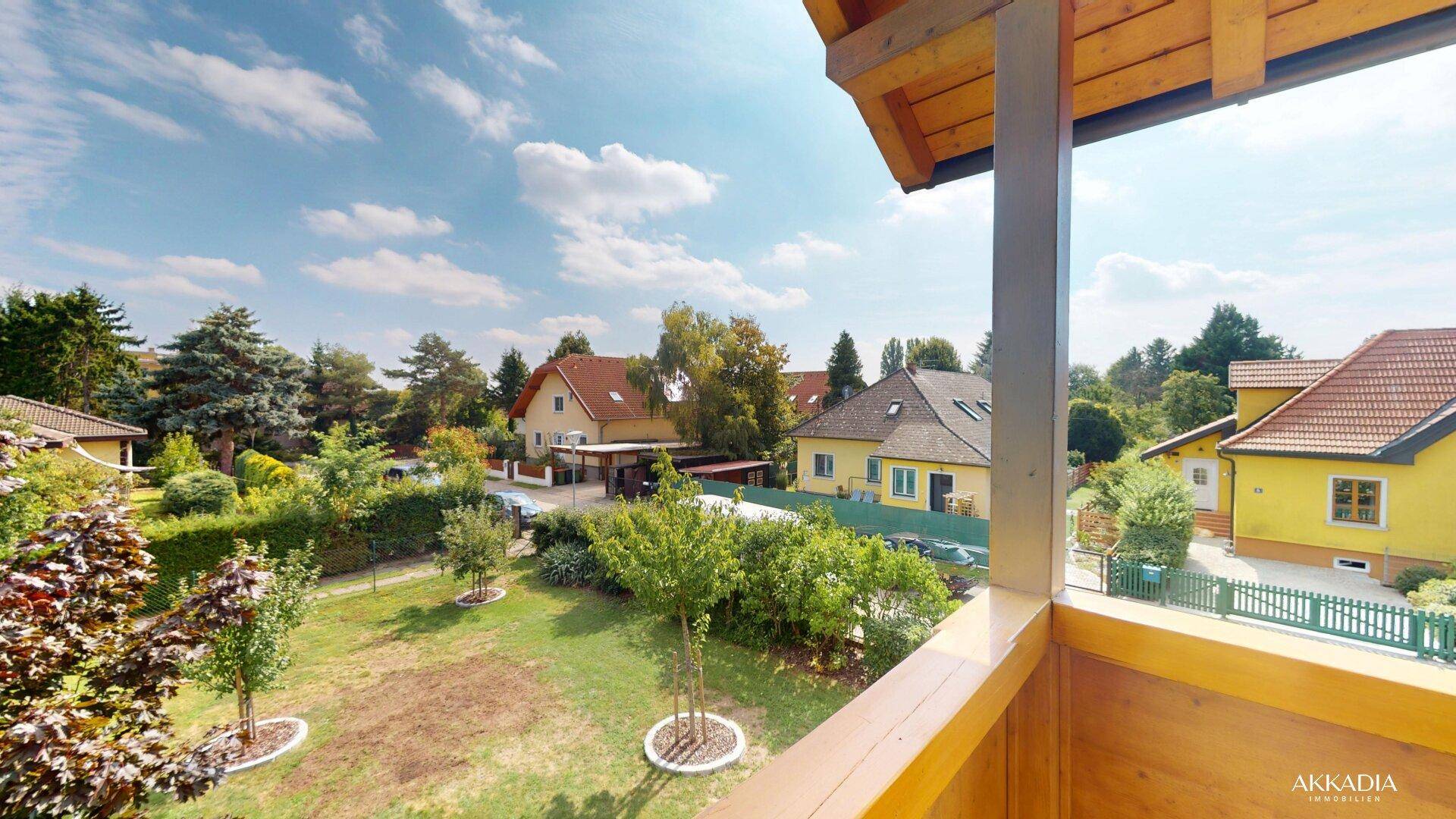 Weitläufiger Blick vom Balkon über den gepflegten Garten und die ruhige Nachbarschaft, unter blauem Himmel.