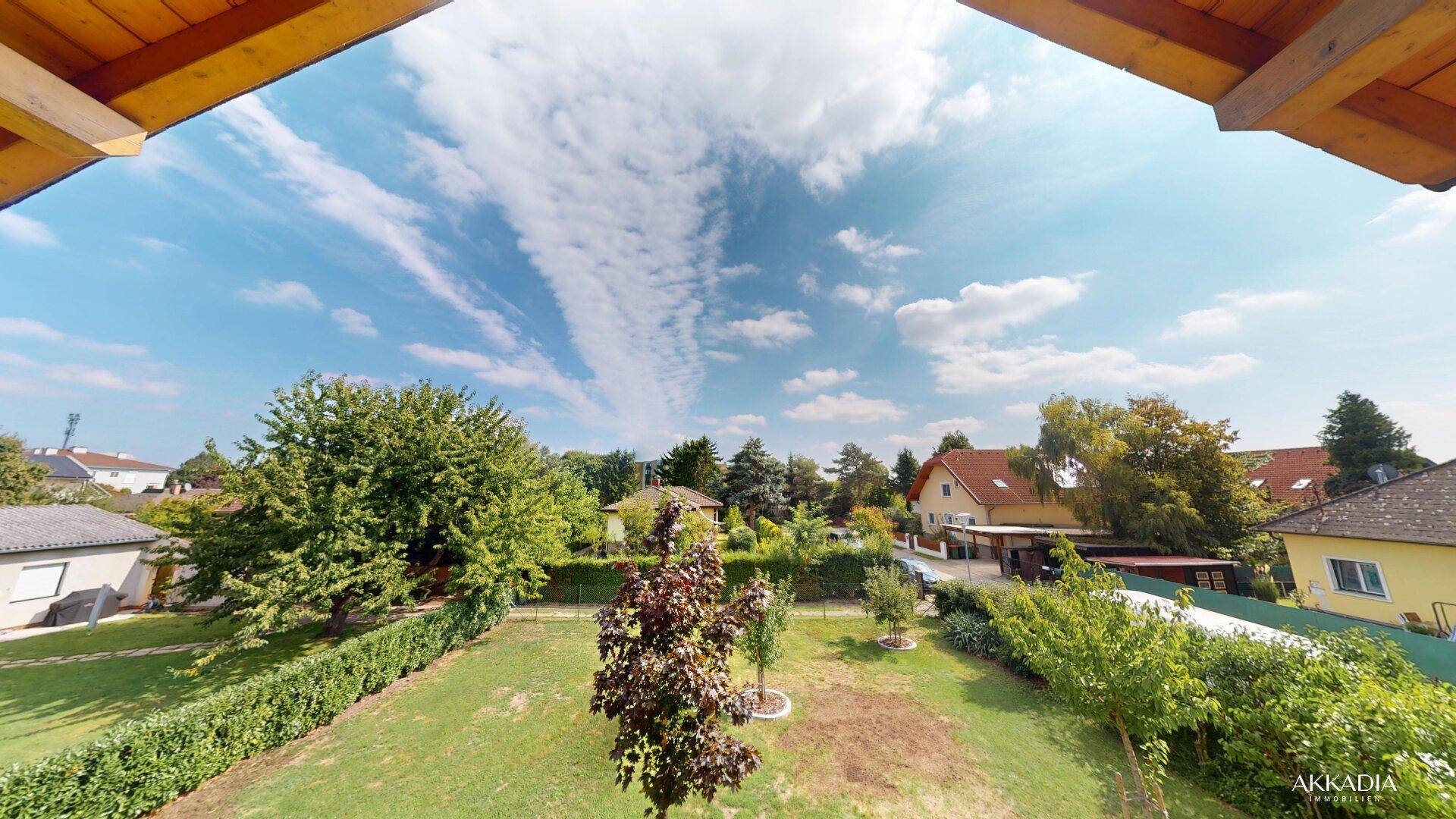 Panoramablick vom Balkon mit weitem Himmel und üppigem Grün der Gärten und Bäume in der Umgebung.