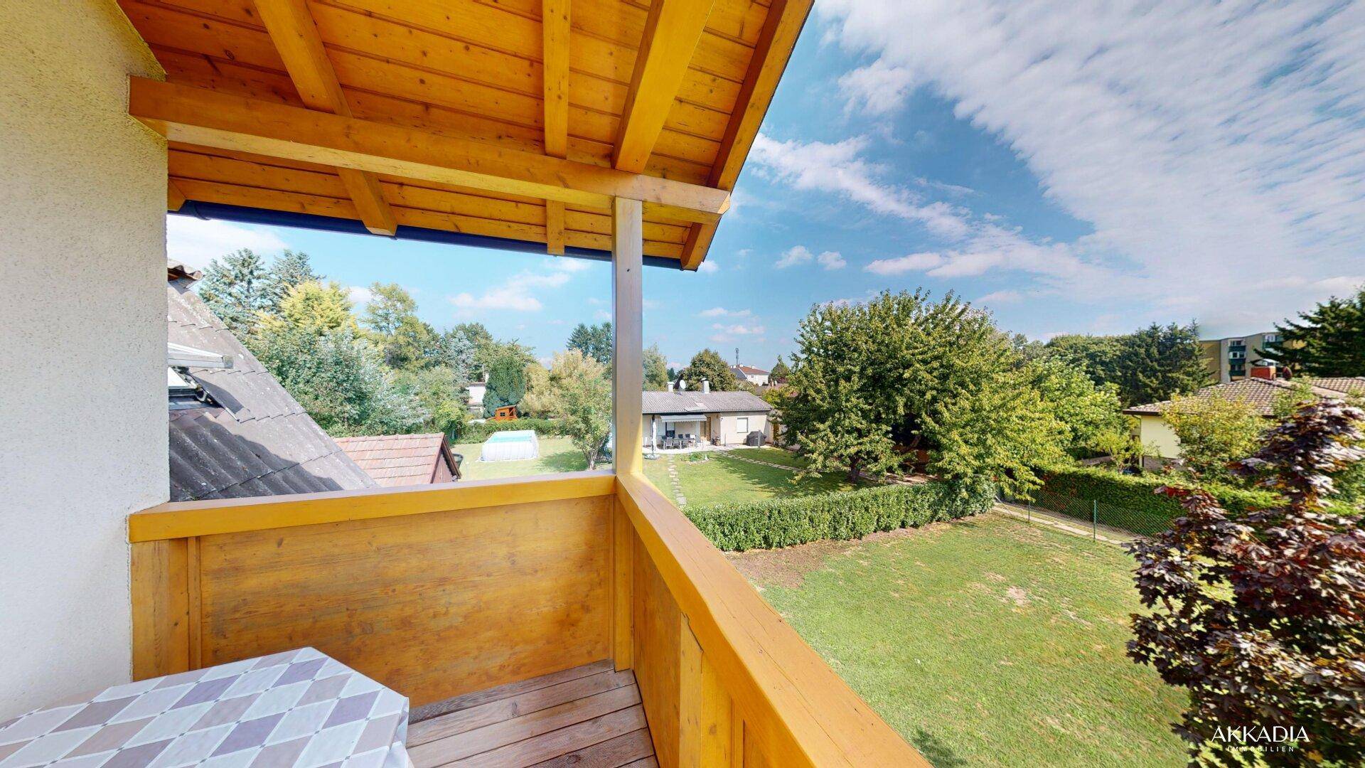 Geräumiger Balkon mit kleinem Tisch und Blick auf den weitläufigen Garten, umgeben von viel Grün.