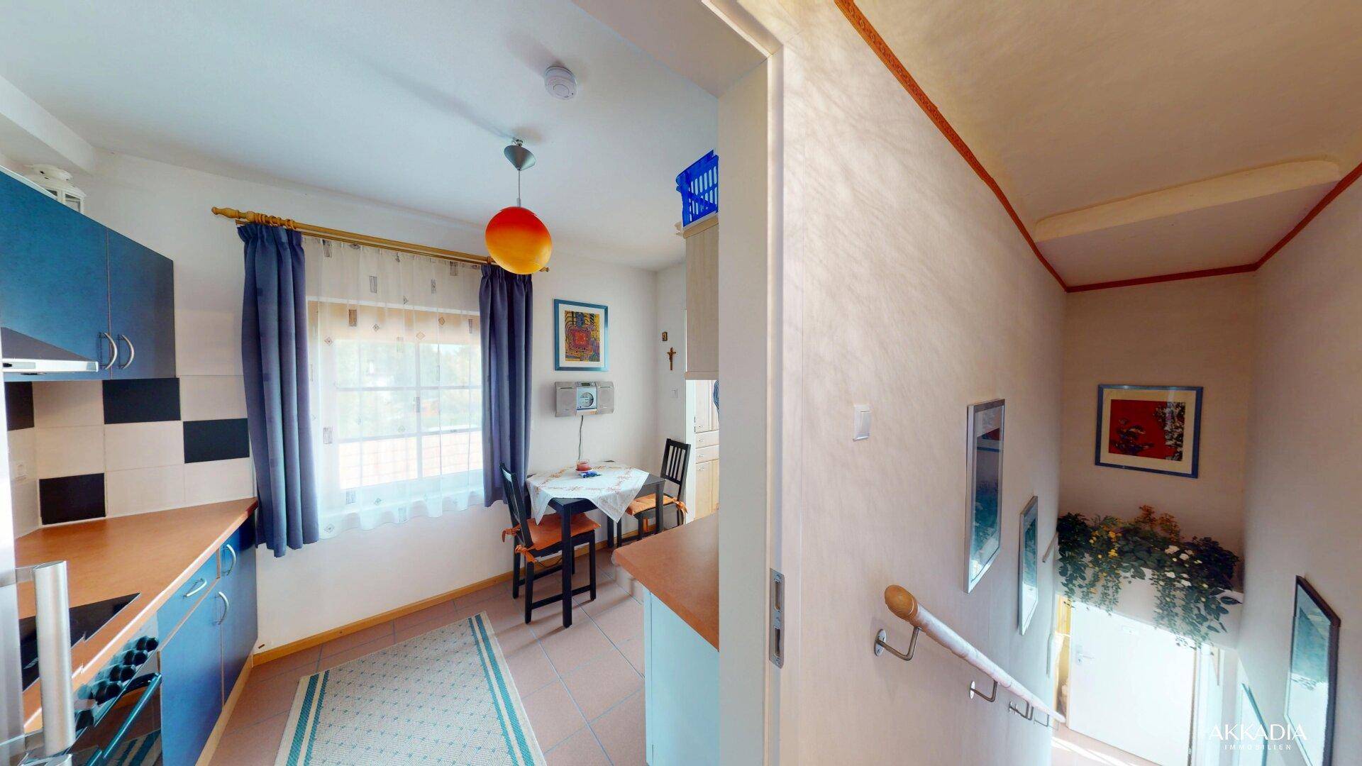 Funktionale Küche mit blauen Schränken, Essbereich am Fenster und Zugang zum Treppenhaus, hell und praktisch.