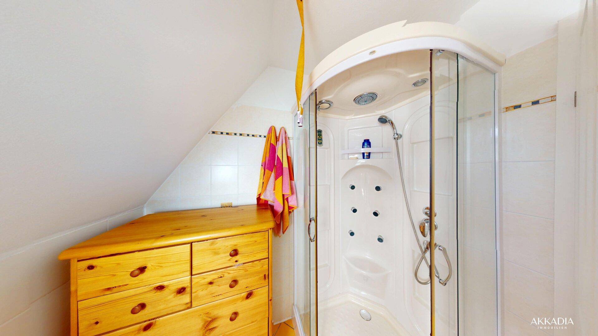 Badezimmer mit Eckduschkabine und rustikaler Holzkommode, unter einer Dachschräge gelegen.