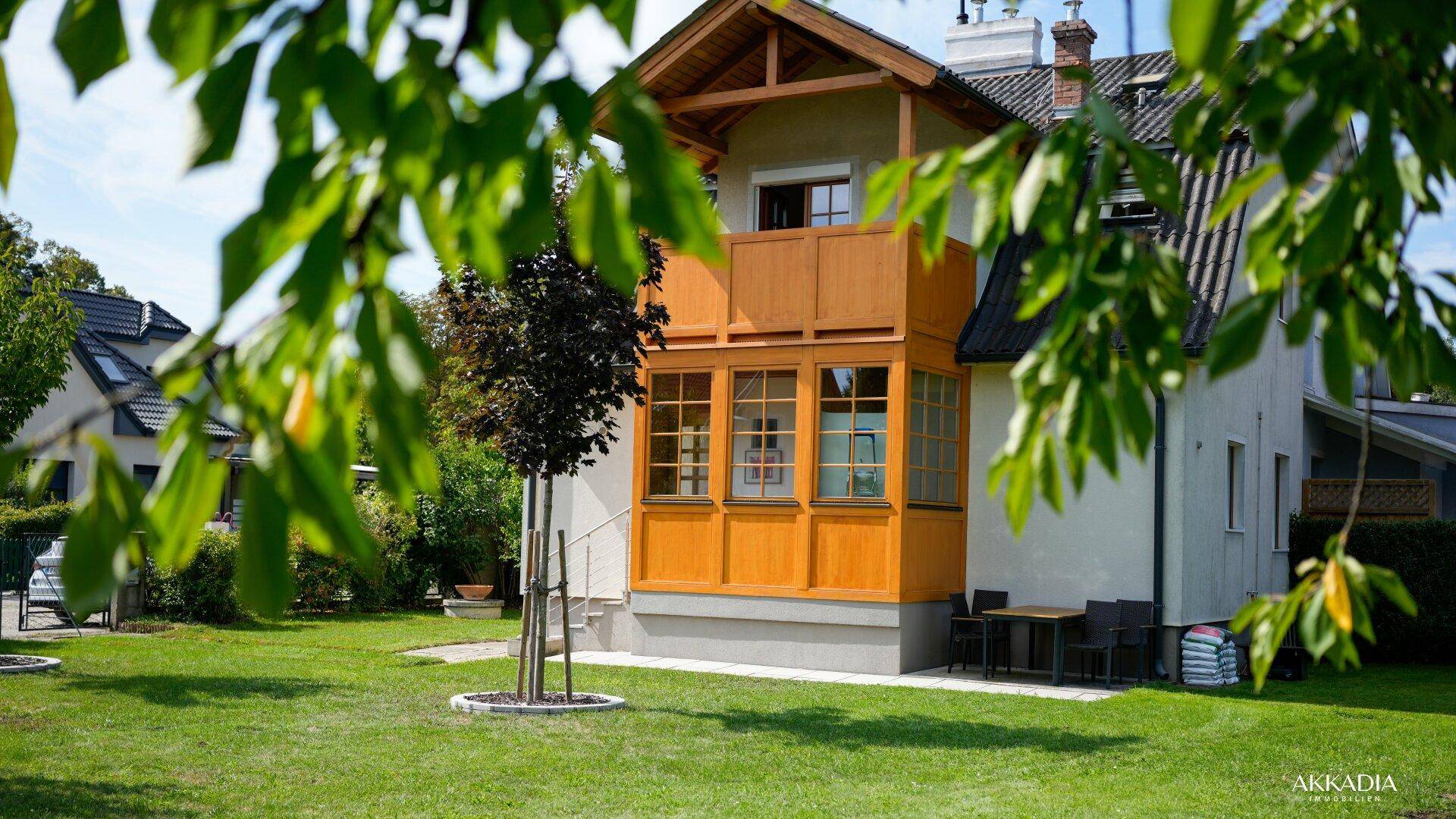Attraktives Einfamilienhaus mit gepflegtem Rasen und Holzdetails an Balkon und Wintergarten, unter blauem Himmel.
