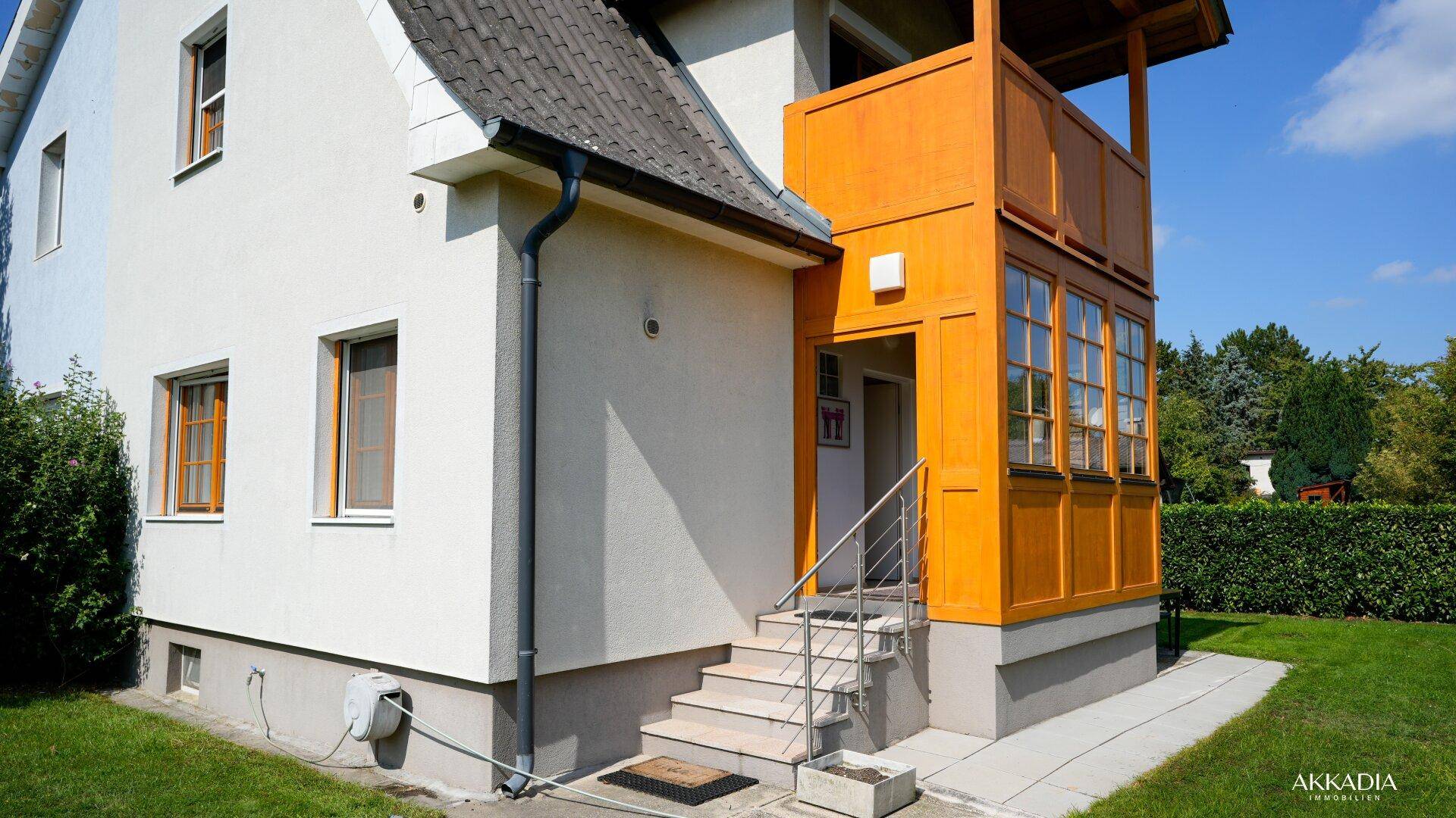 Eingangsbereich des Hauses mit Außentreppe und traditioneller Holzverkleidung unter blauem Himmel.