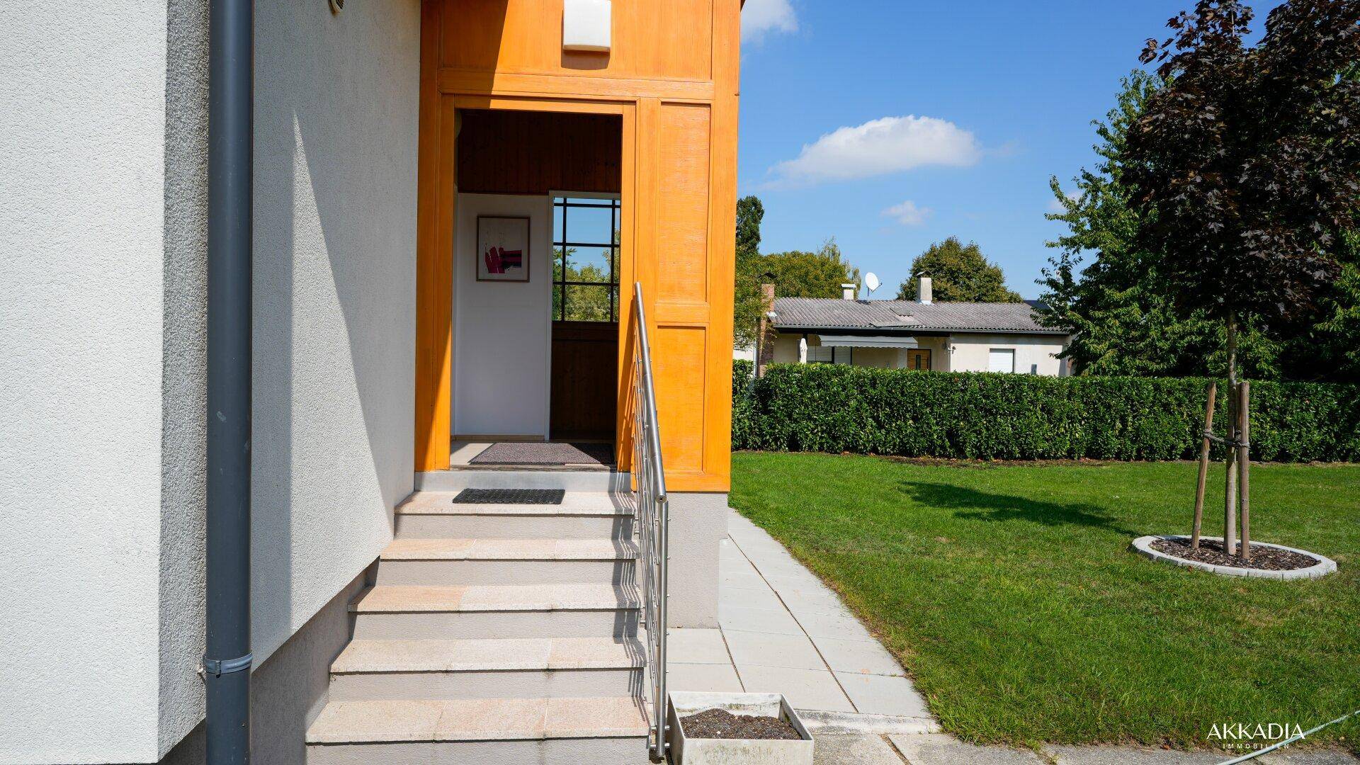 Eingangsbereich des Hauses mit Steintreppe und Geländer, umgeben von einem gepflegten Vorgarten.