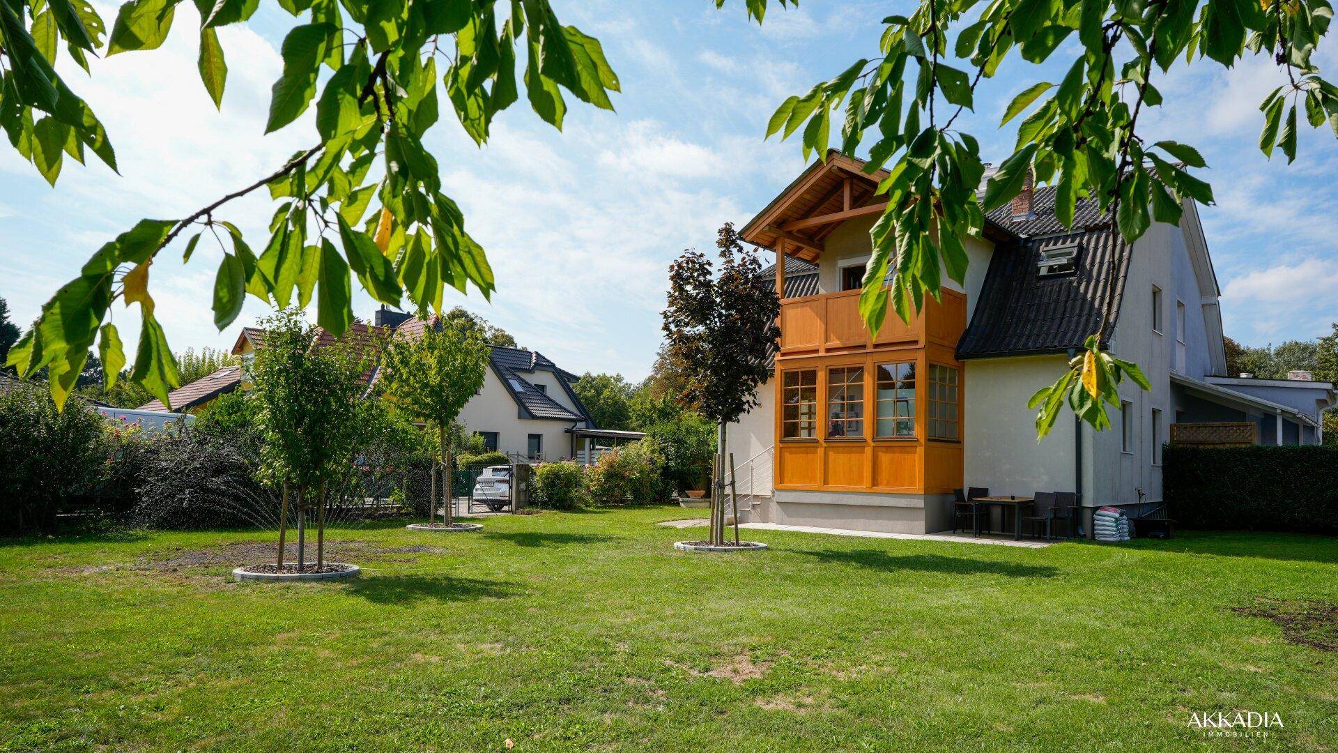 Charmantes Haus mit Holzverkleidung, Balkon und großem Garten, umgeben von grünen Bäumen.