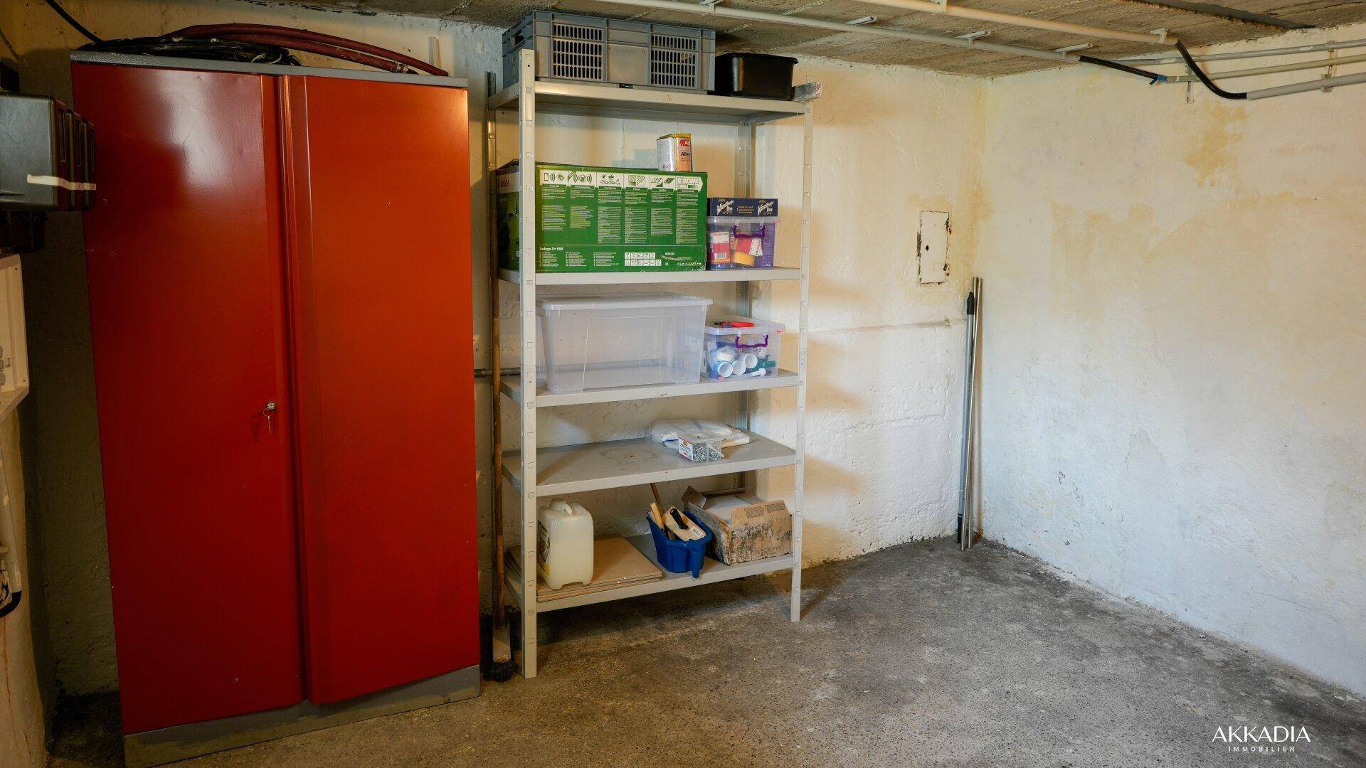 Kellerraum mit rotem Metallschrank und Metallregalen für zusätzlichen Stauraum.