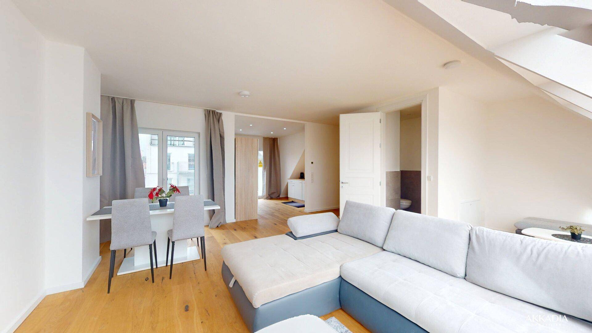 Heller Wohn-Essbereich mit bequemer Couch, Esstisch und Zugang zu einem weiteren Zimmer.