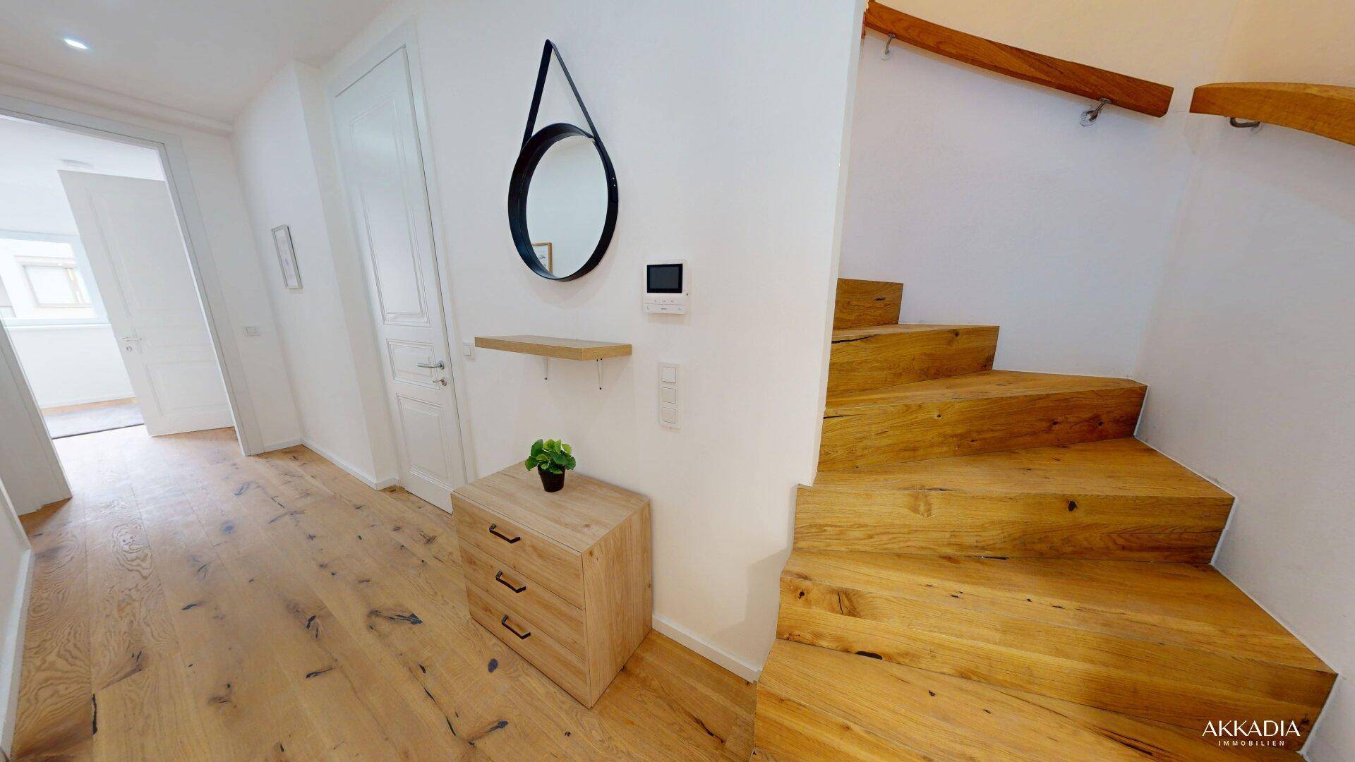Heller Flur mit Holztreppe, Holzboden und modernem Spiegel an der Wand.