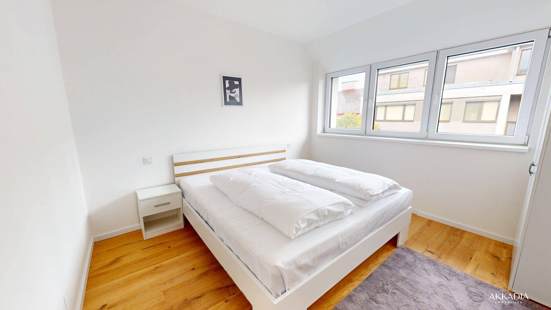 Helles Schlafzimmer mit Holzboden, Doppelbett und großen Fenstern mit Blick nach draußen.