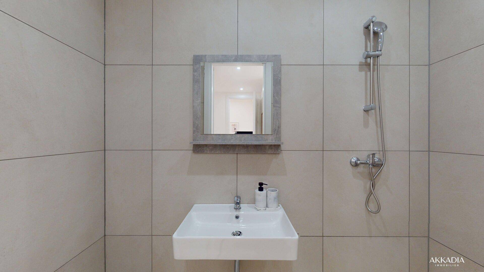 Modernes Badezimmer mit grauen Fliesen, Waschbecken und Duscharmatur.