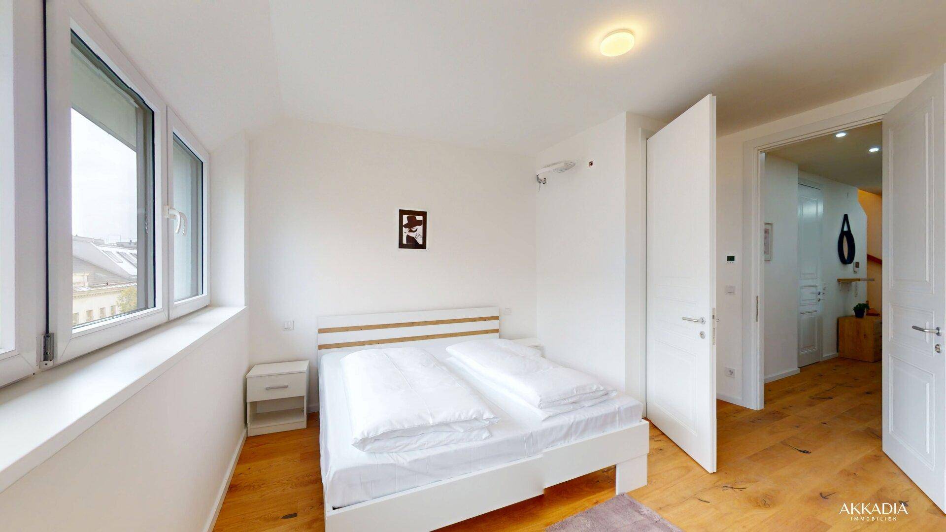 Schlafzimmer mit Holzboden, Doppelbett und Zugang zu einem hellen Flur.