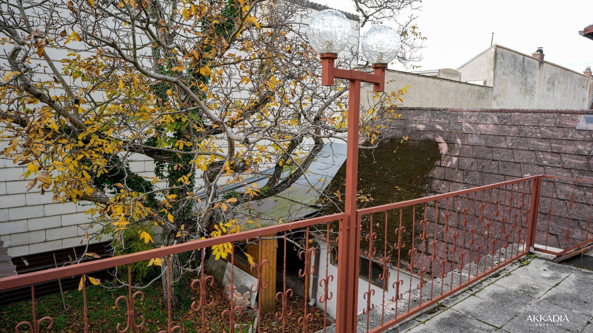Ausblick von der Terrasse über ein Nebengebäude und herbstliche Bäume.