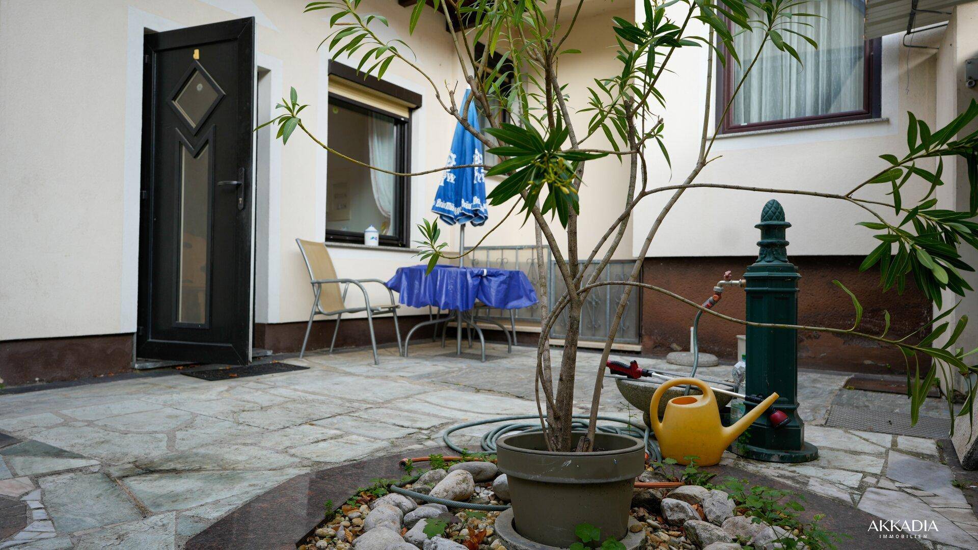 Gemütlicher Innenhof mit einem kleinen Baum, Sitzgelegenheiten und einem Sonnenschirm.