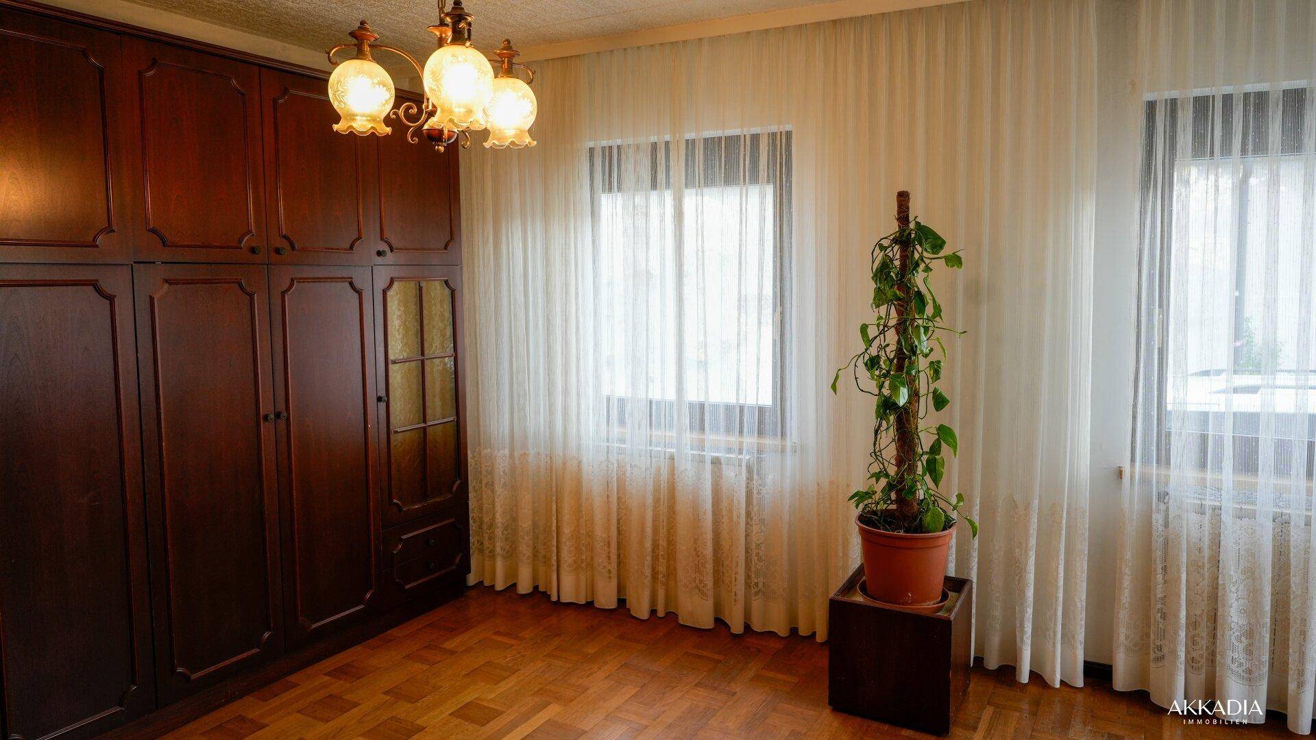 Schlafzimmer mit großen Einbauschränken, Parkettboden und hellen Vorhängen.